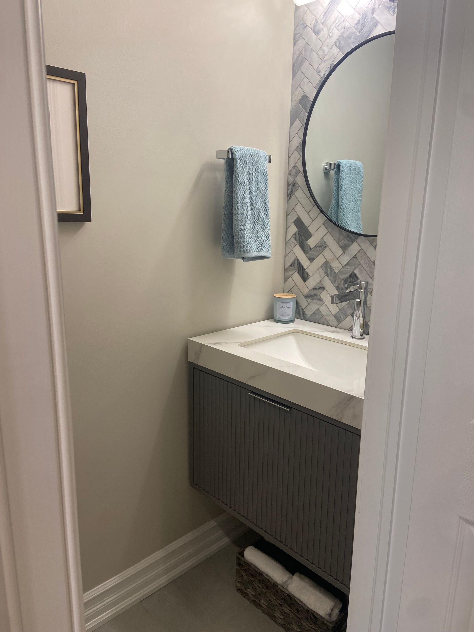 Modern bathroom vanity with white sink, round mirror, blue towel, and patterned backsplash.