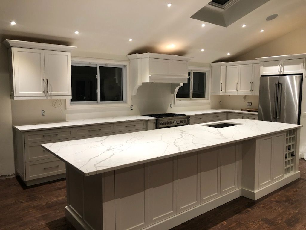 Bright modern white kitchen with large island, stainless appliances, and dark wood floors