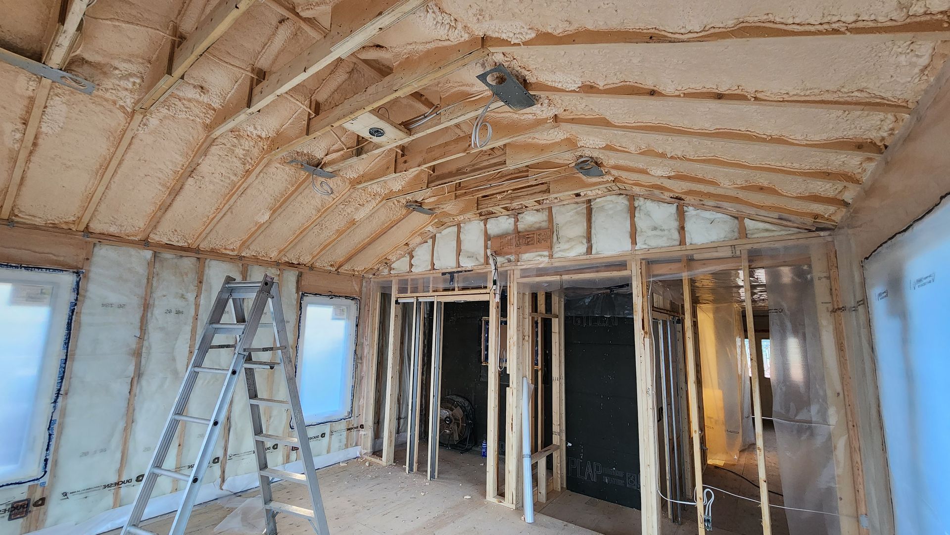Partially renovated room with exposed ceiling insulation, framing studs, and a ladder by the wall