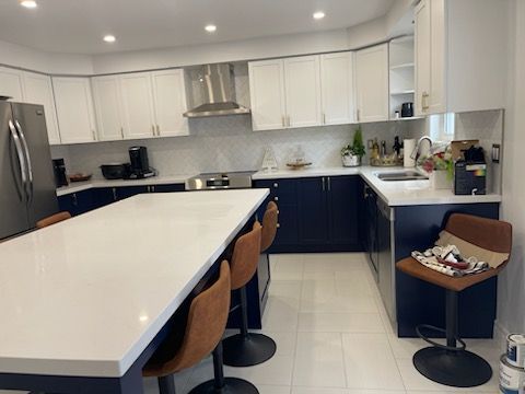 Bright modern kitchen with white island, navy cabinets, bar stools, and stainless steel appliances