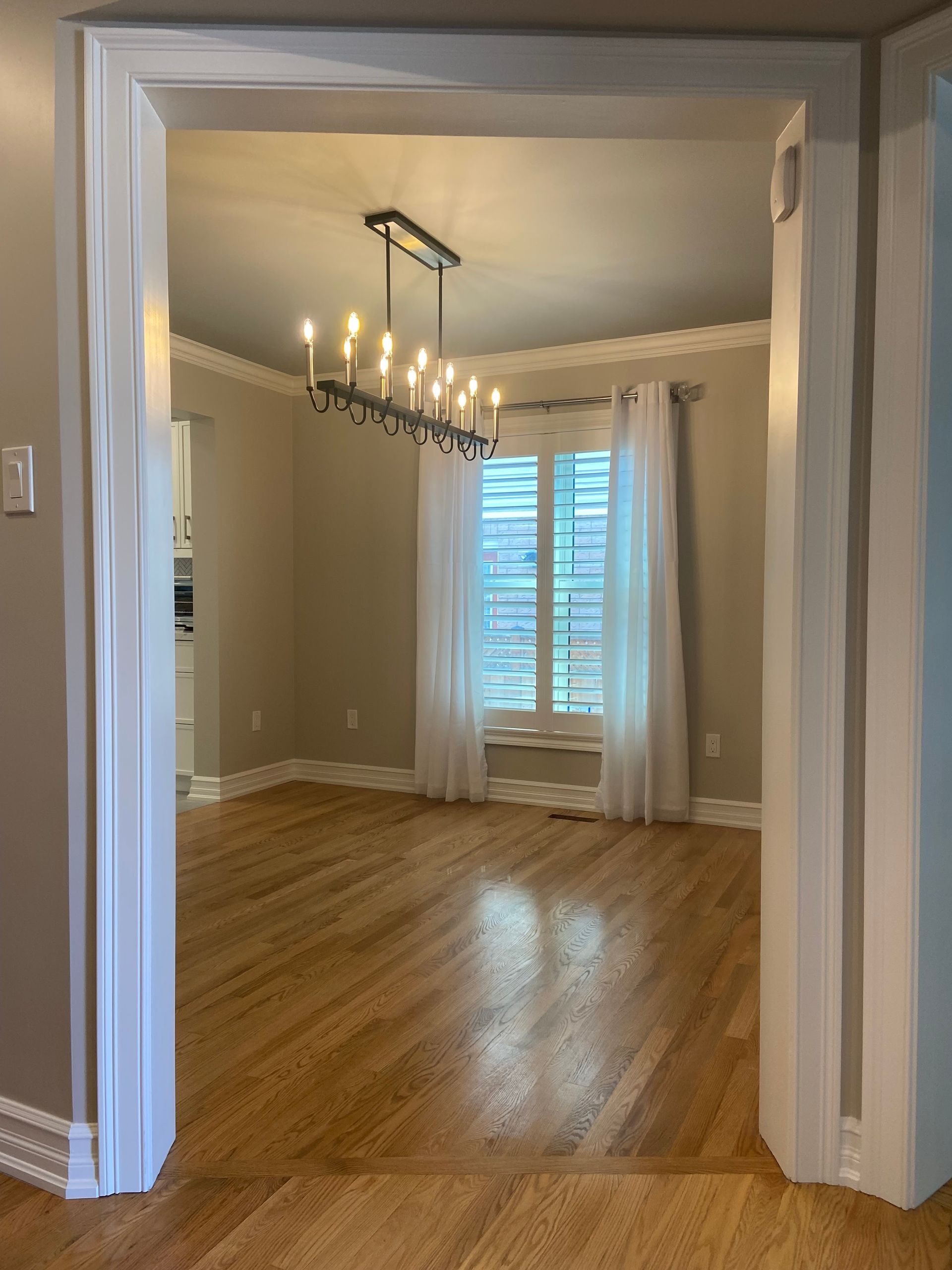Empty dining room with hardwood floors, neutral walls, chandelier, and window with sheer curtains