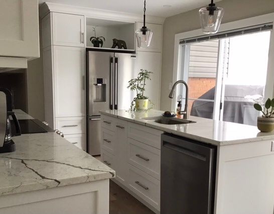 Modern white kitchen with stainless steel refrigerator, island sink, and marble countertops