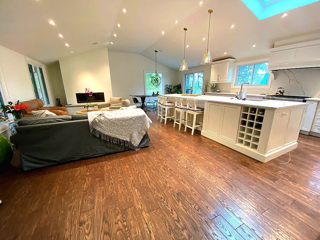 Open-plan living room and kitchen with wood floors, white island, and gray sectional sofa under skylights