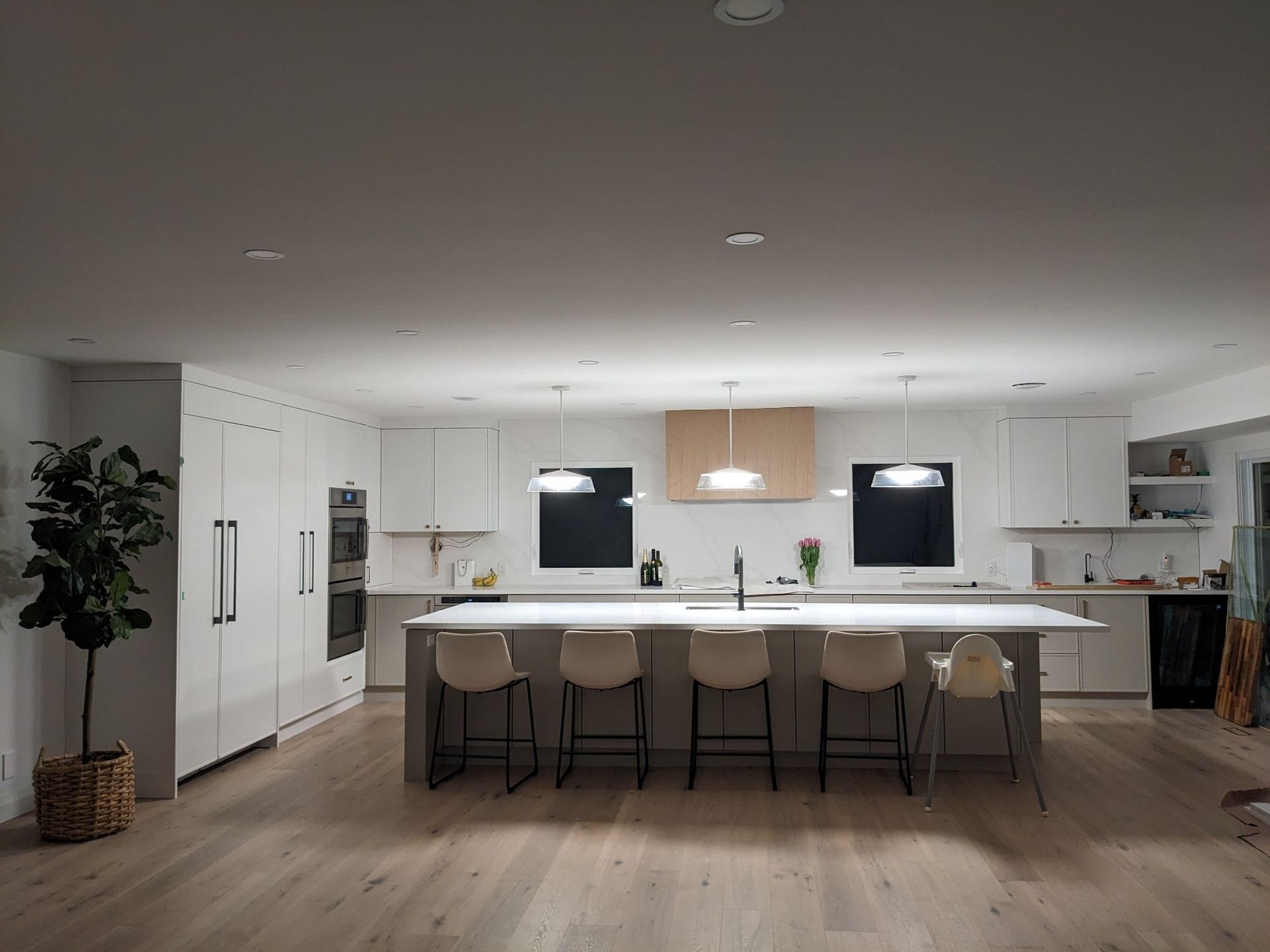 Modern white kitchen with island seating, wood floors, and recessed lighting