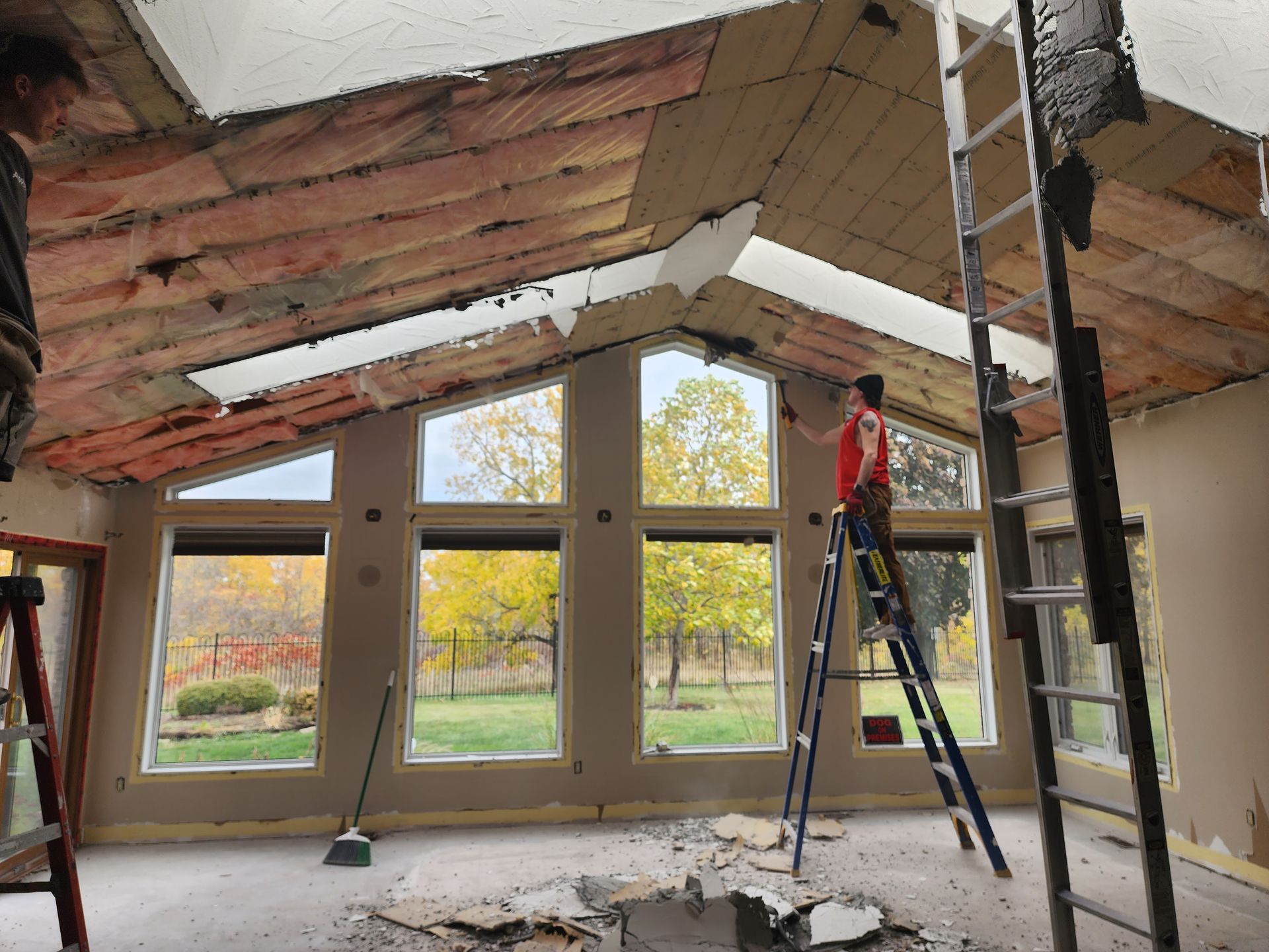 Worker on a ladder in a room with a partially removed ceiling and exposed beams during renovation