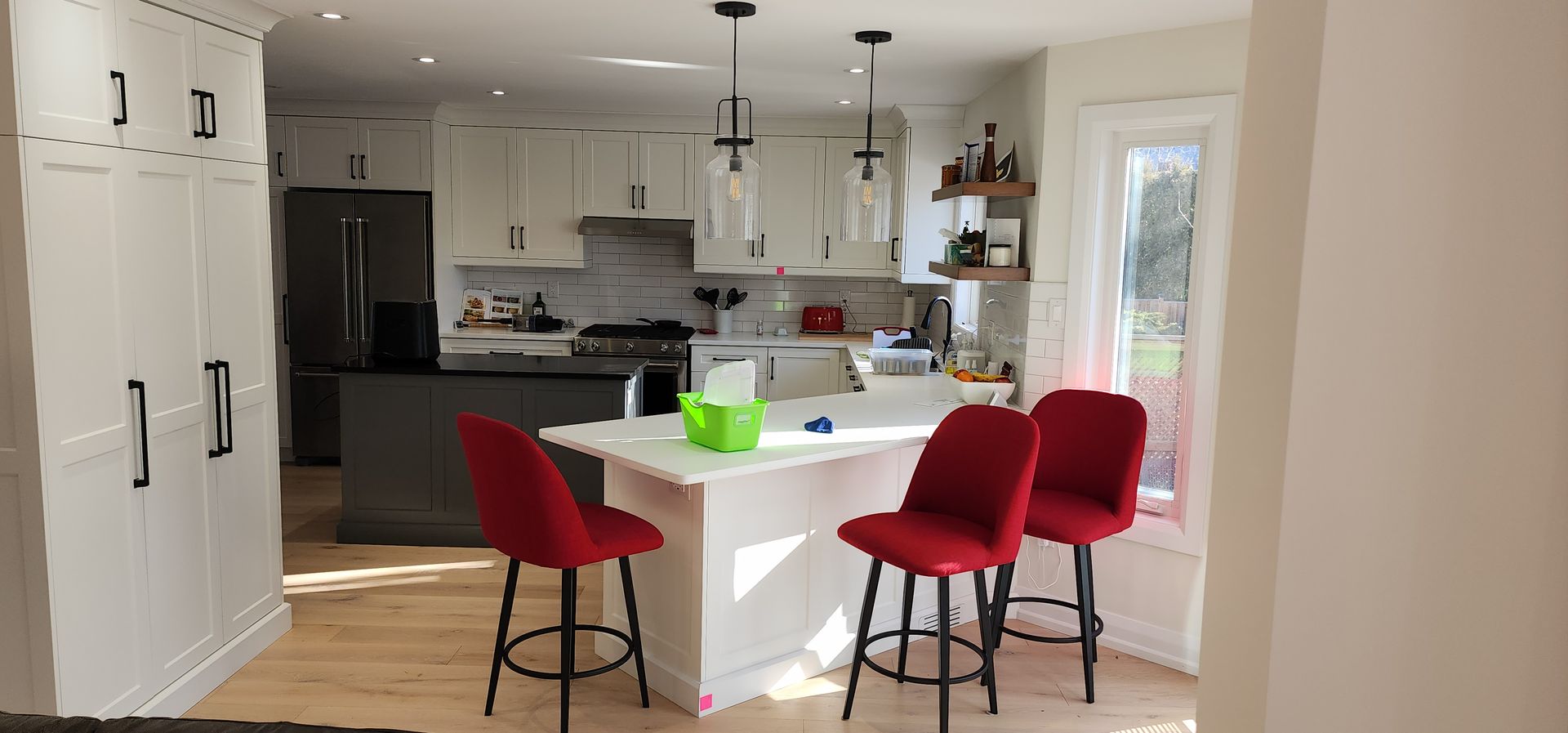 Modern kitchen with white island, red barstools, and a green vase on the counter.
