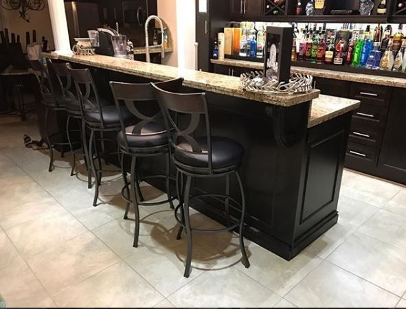 Home bar area with stools, black cabinetry, granite counter, and bottles on display