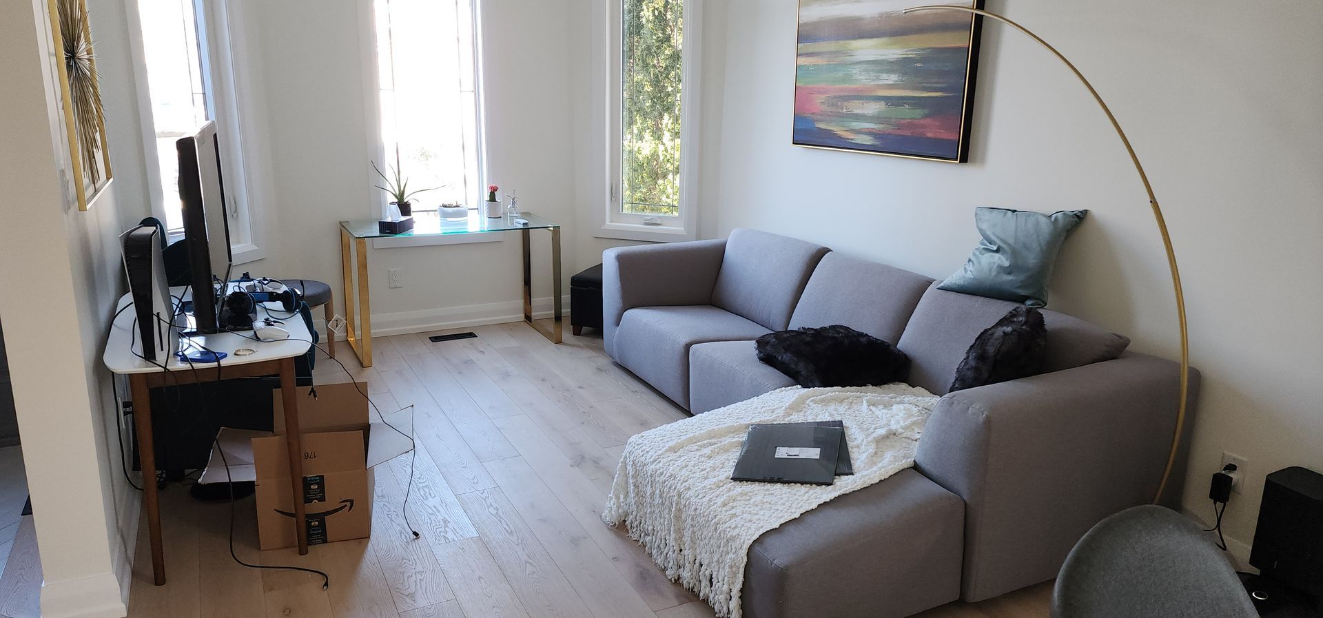 Small living room with gray sectional, desk by window, TV on stand, and arched floor lamp