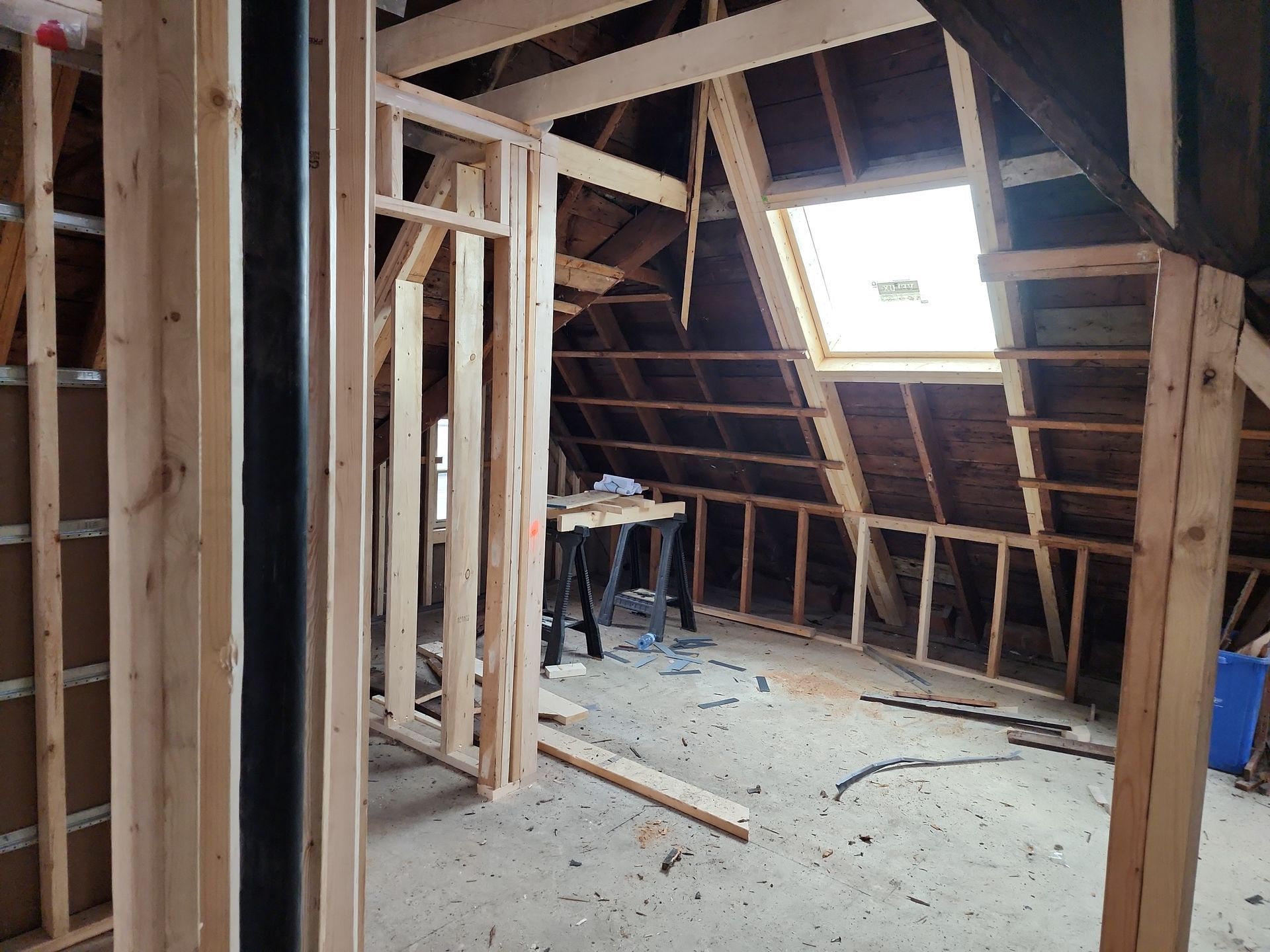 Attic under renovation with exposed wooden framing, a skylight, and construction debris on the floor