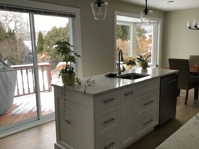 Bright kitchen with a white island, sink, and large windows overlooking a snowy deck and yard.