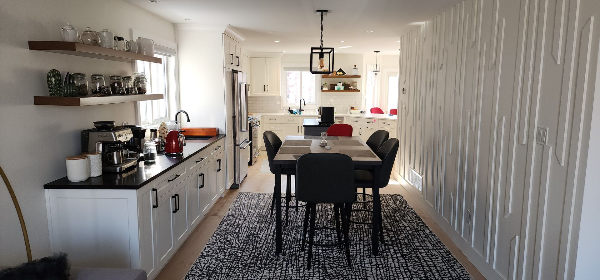 Modern kitchen and dining area with black table, chairs, patterned rug, and white cabinets