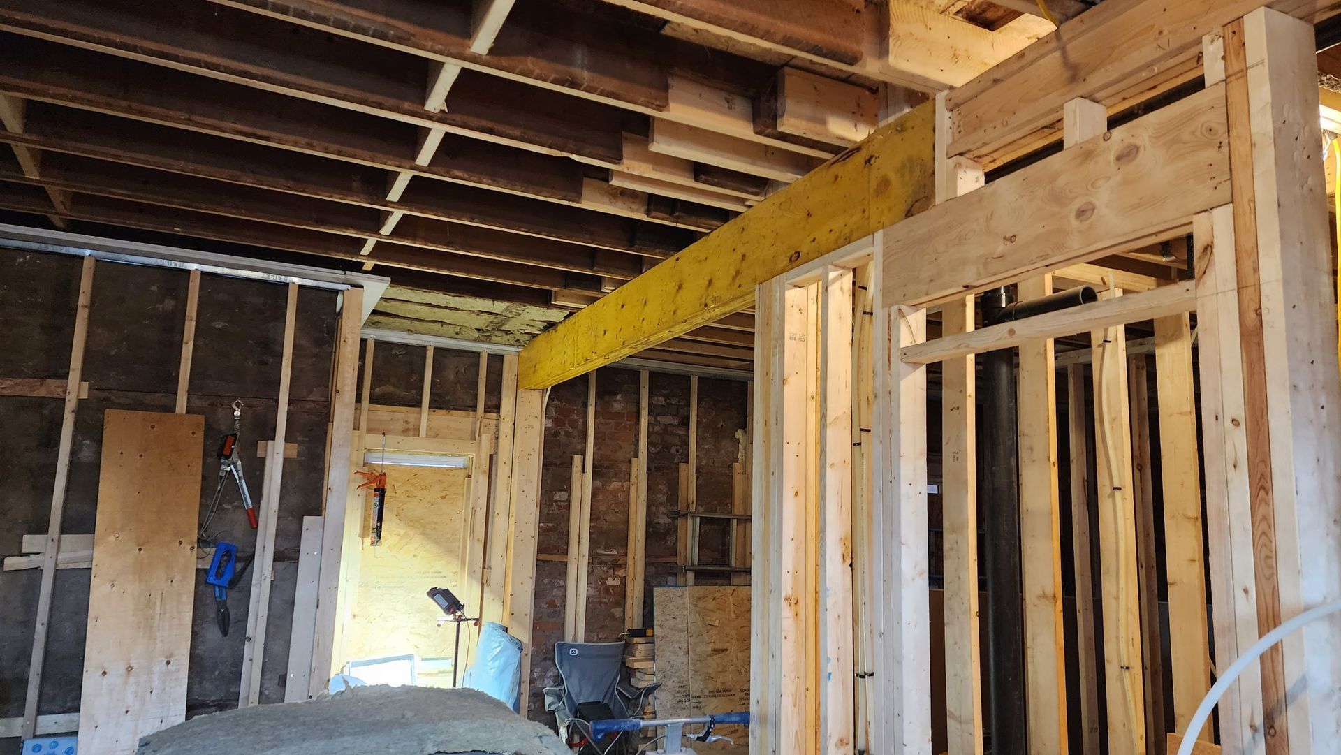 Unfinished interior with exposed wooden framing, ceiling joists, and construction materials in a partially built room