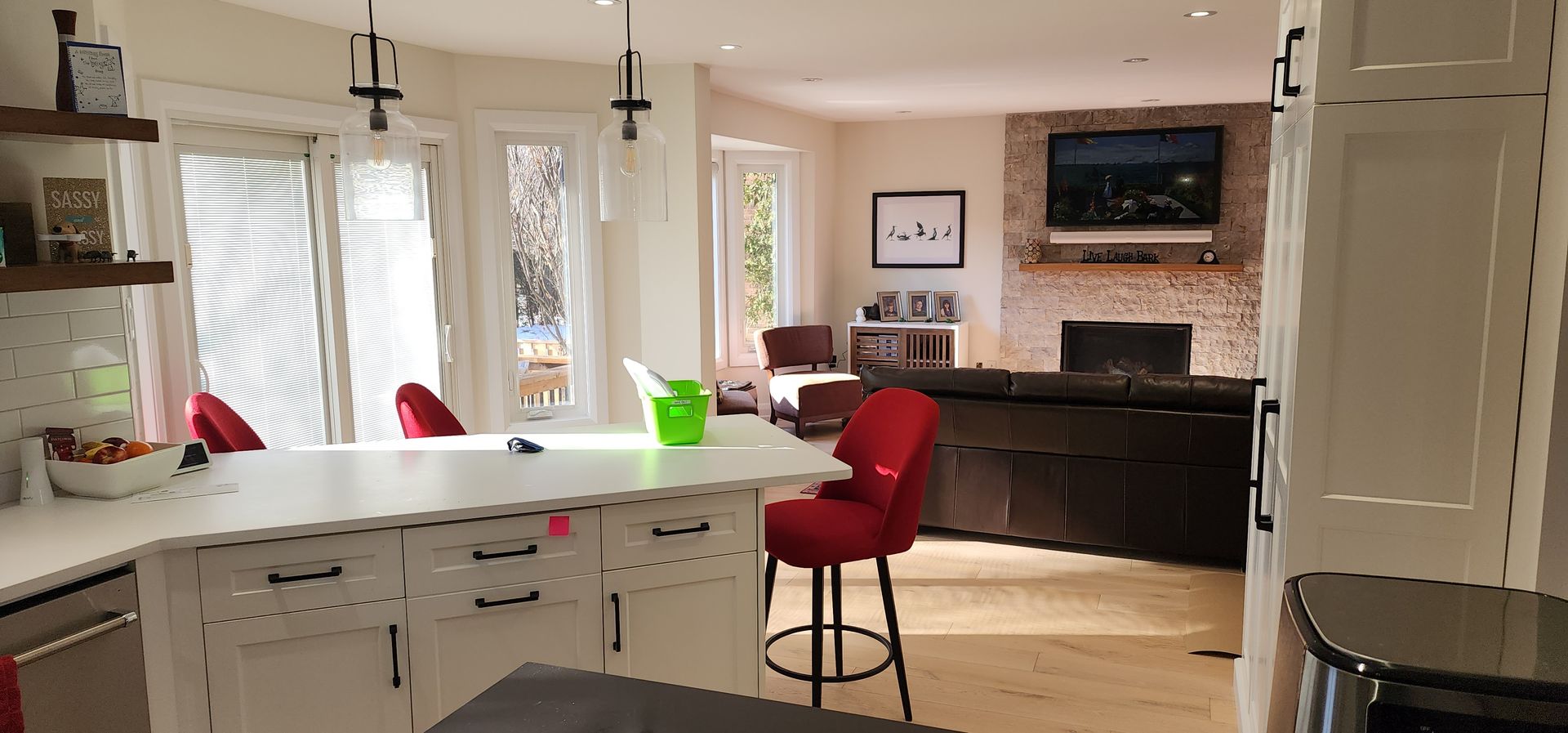 Bright modern kitchen with white island, red stools, dark cabinets, and a wall-mounted TV in the background