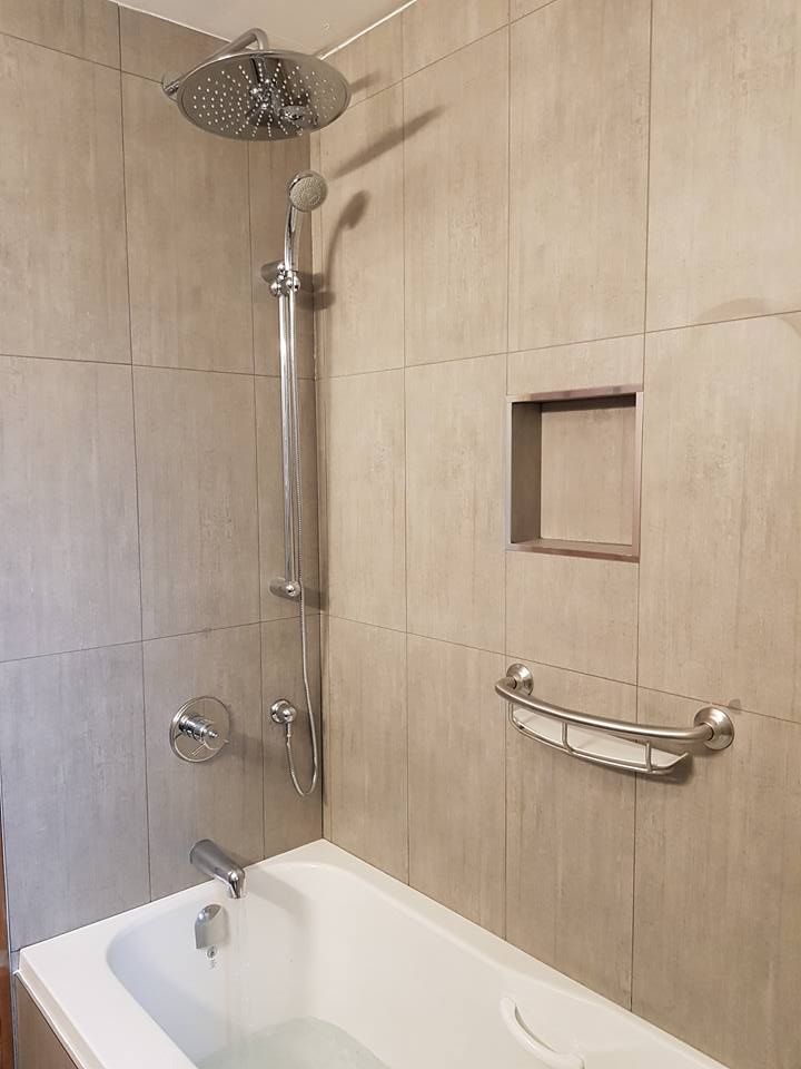 Accessible shower and bathtub with grab bars, handheld showerhead, and beige tile walls