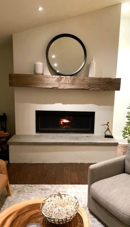 Modern living room fireplace with wood mantel, round mirror, and neutral furniture