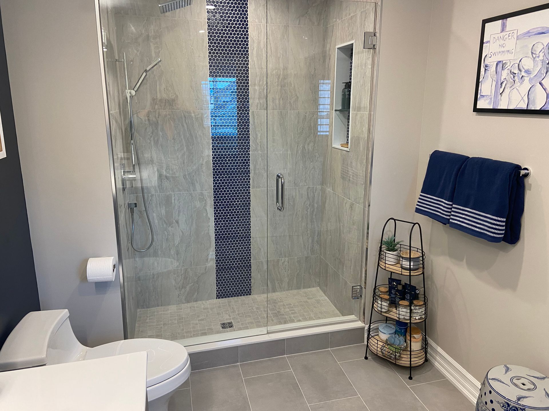 Modern bathroom with glass shower, white toilet, tiled floor, and blue towel on wall rack