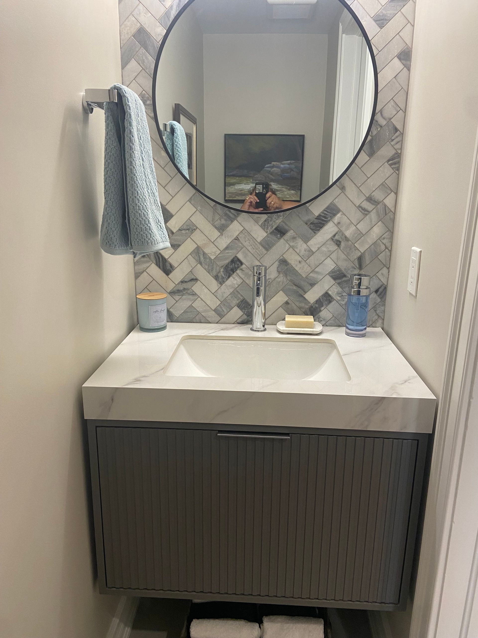 Modern bathroom vanity with round mirror, gray tile backsplash, white sink, and hanging towel