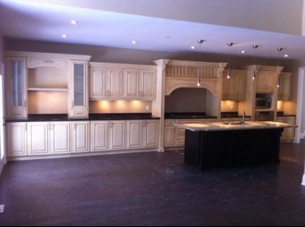 Empty kitchen with white cabinets, dark island, and built-in oven under warm recessed lighting