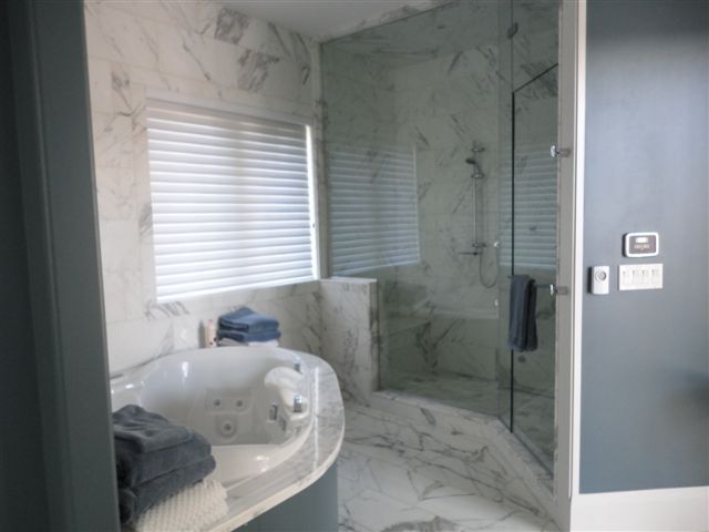 Modern bathroom with white marble tile, glass shower, and a large tub by a window