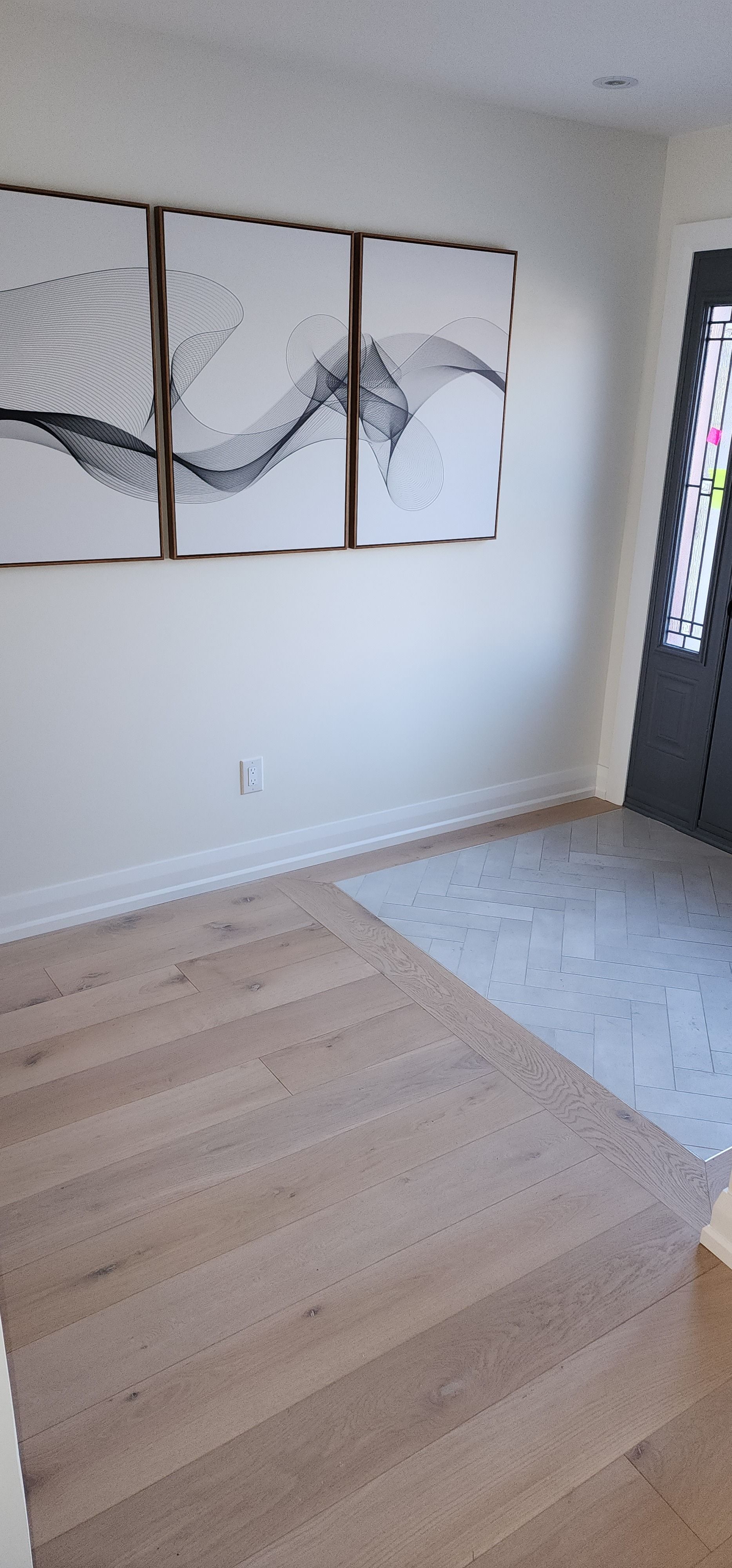 Bright empty entryway with light wood floors, white walls, abstract wall art, and a dark front door with sidelights