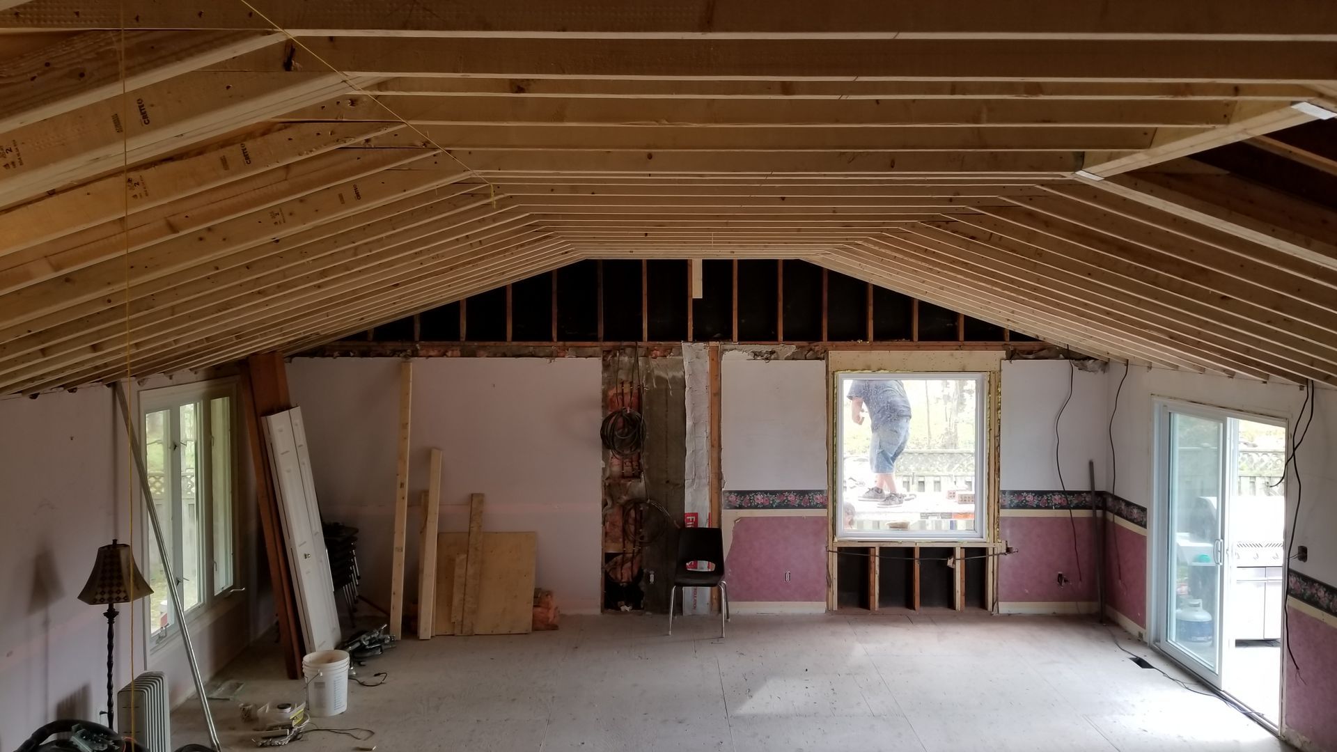 Interior of an unfinished room with exposed rafters, drywall, and open doors and windows.