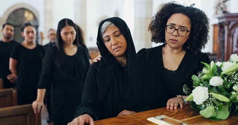 Mourners gathered around a coffin with white flowers during a solemn funeral service.