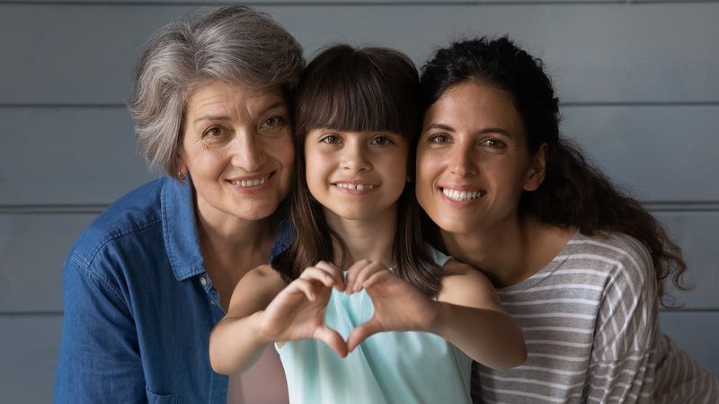 Three people smiling on a couch, with the center person making a heart shape with their hands.
