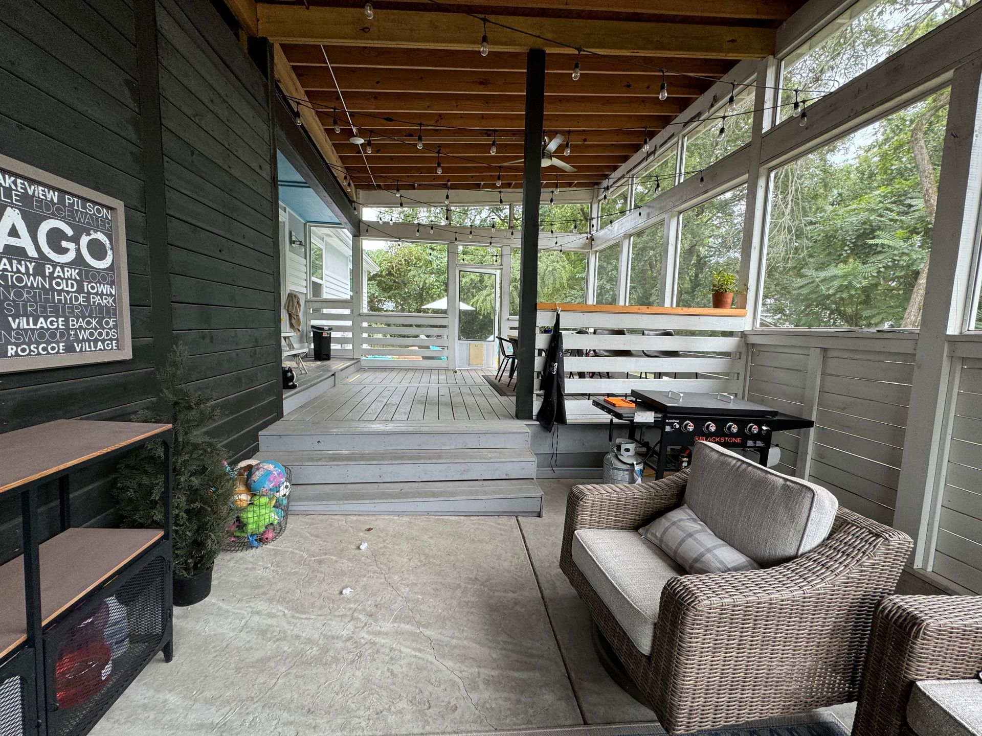 Screened-in porch with gray siding, seating, and a grill; Chicago sign on the wall.