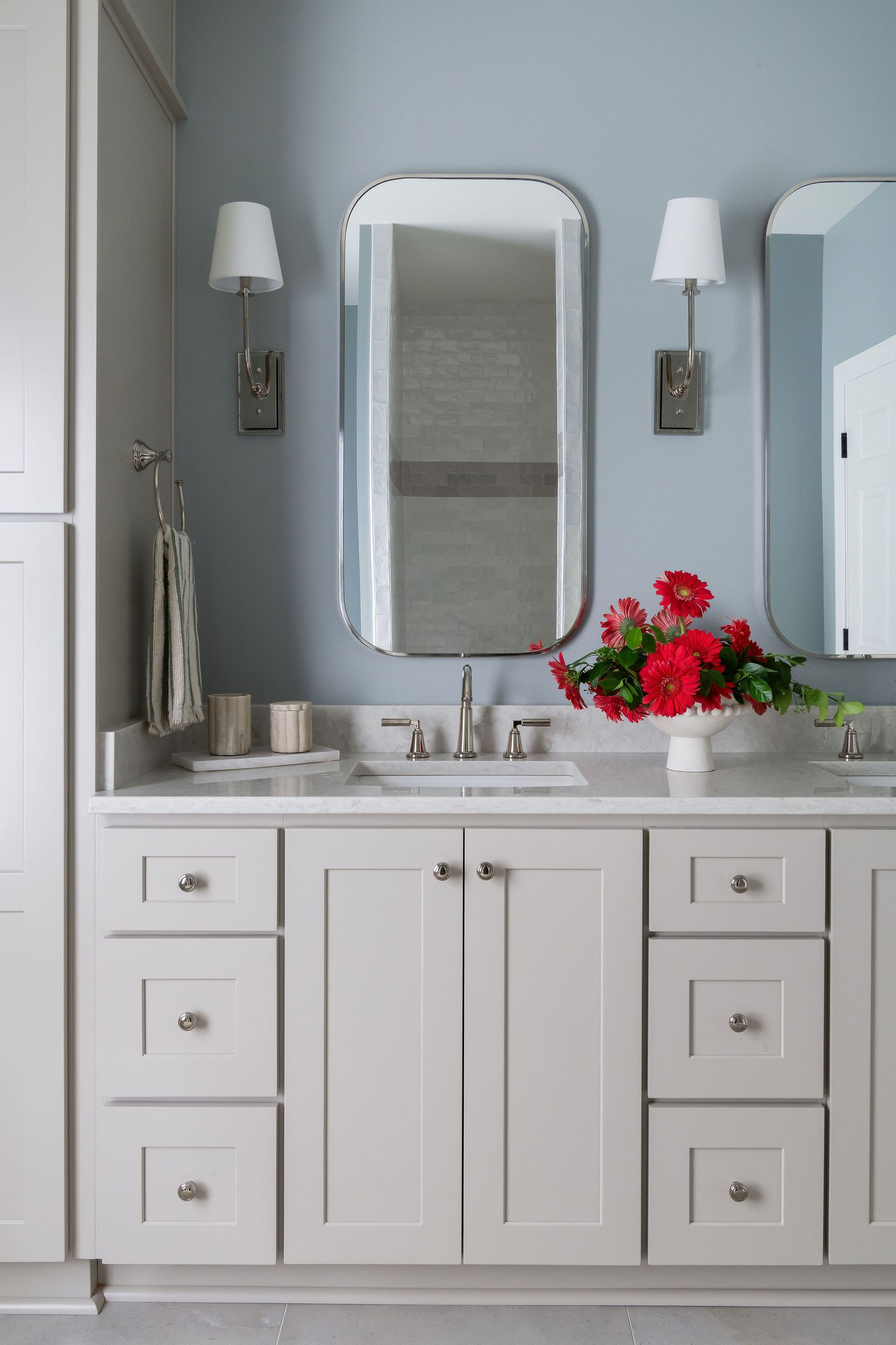 Light gray bathroom vanity with two mirrors, blue walls, and red flowers.
