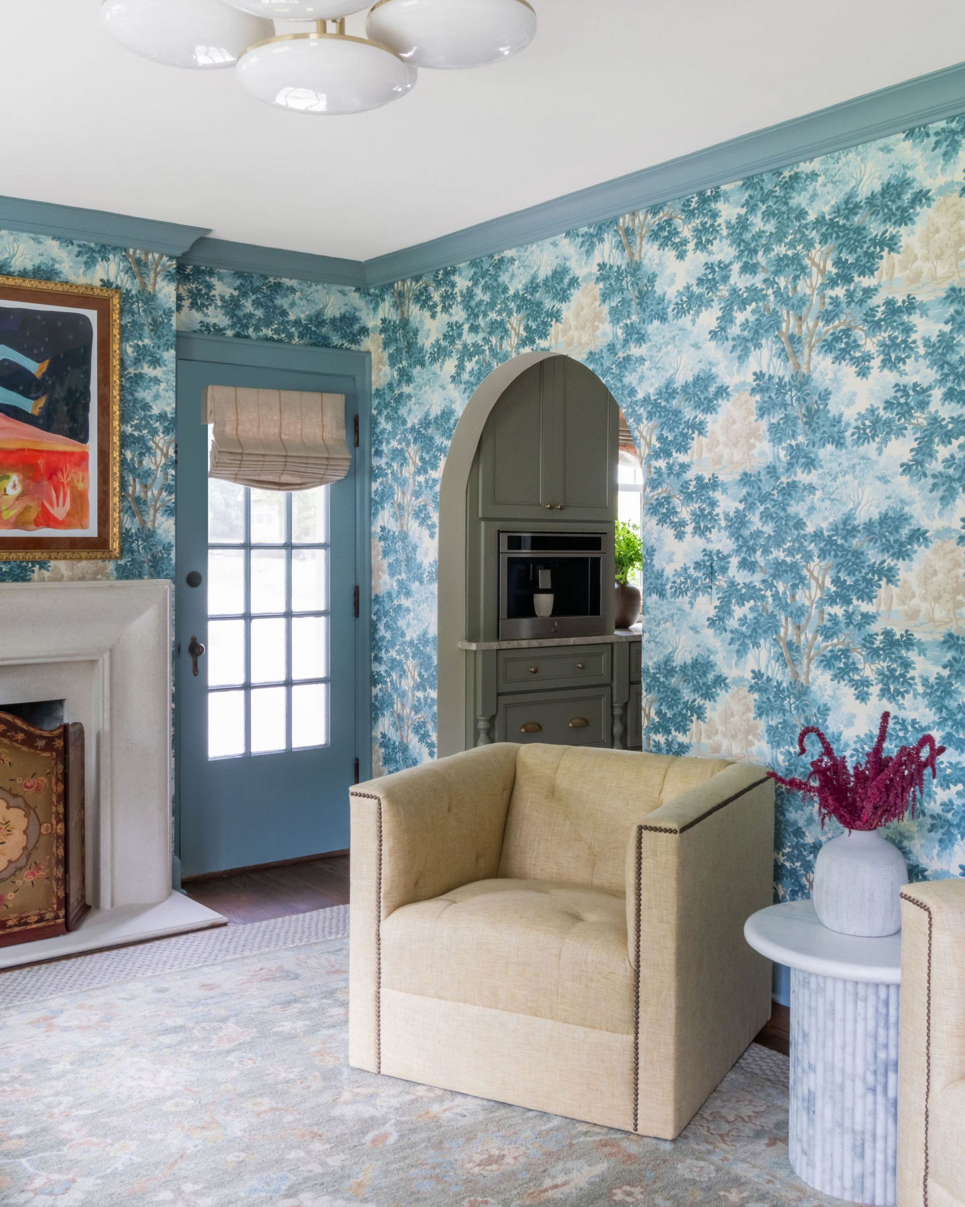 Elegant blue floral wallpaper, beige armchair, and chandelier in a bright living room with an arched doorway.