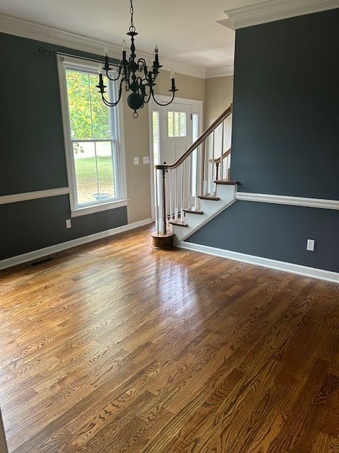 Hardwood-floored room with dark gray walls, white trim, and a staircase leading to a front door with glass panels.