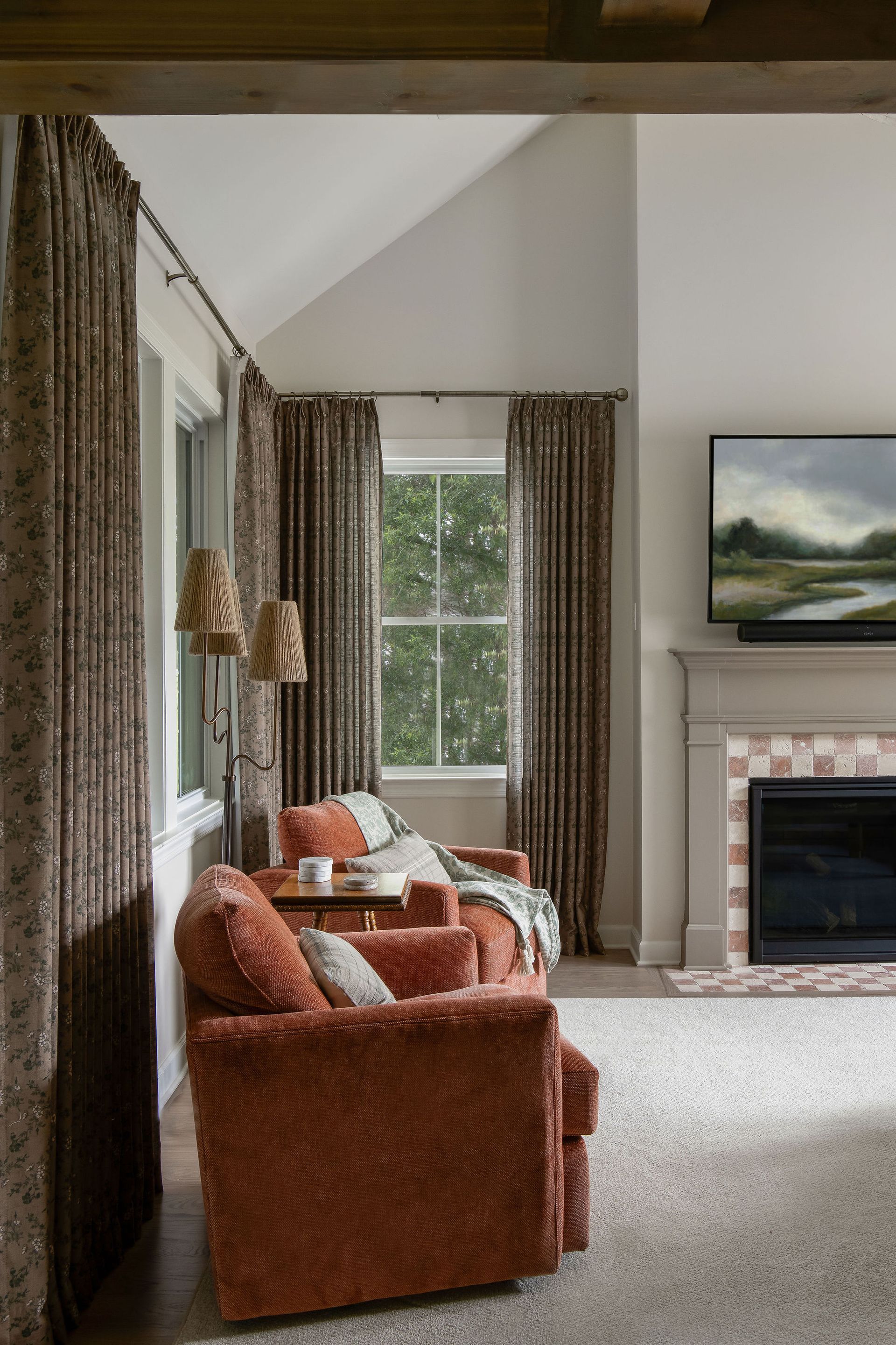 Living room with orange chairs, fireplace, patterned curtains, and a window.