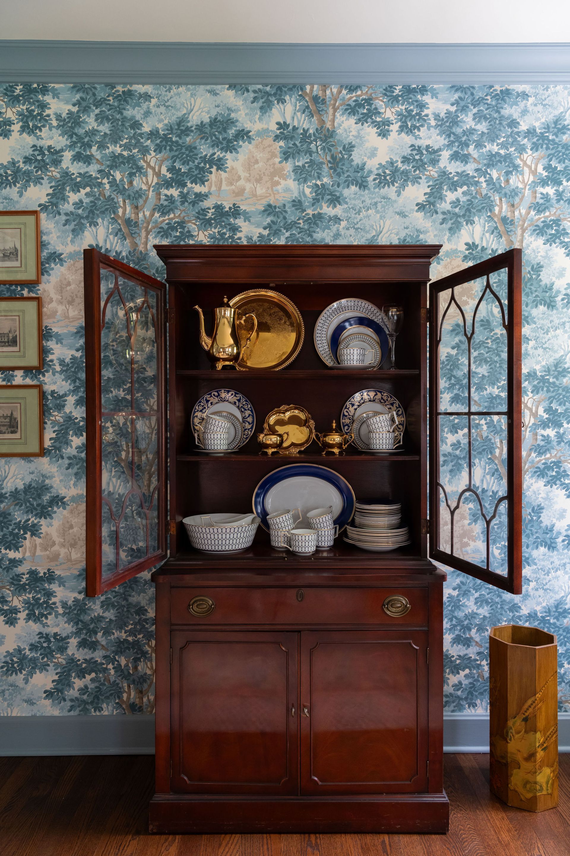 Open wooden hutch with dishes against blue floral wallpaper
