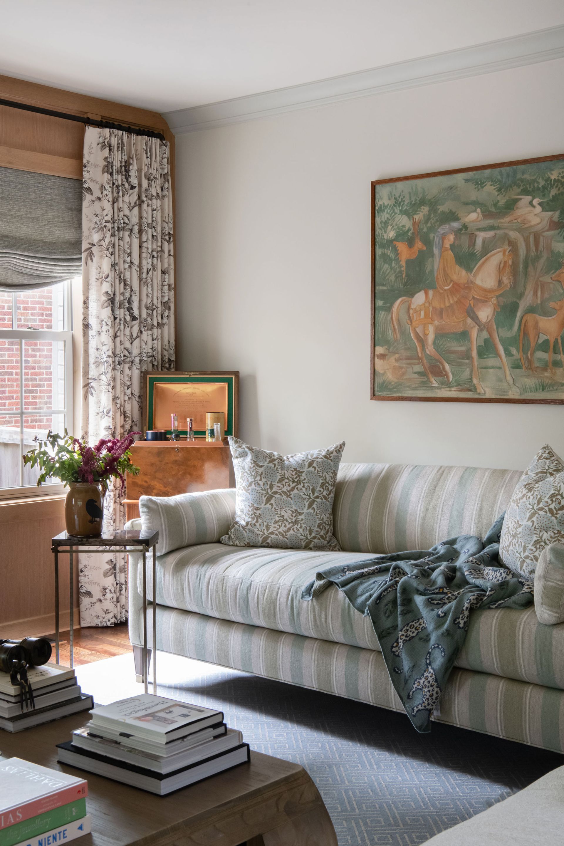 Living room with striped sofa, floral curtains, artwork, and coffee table.