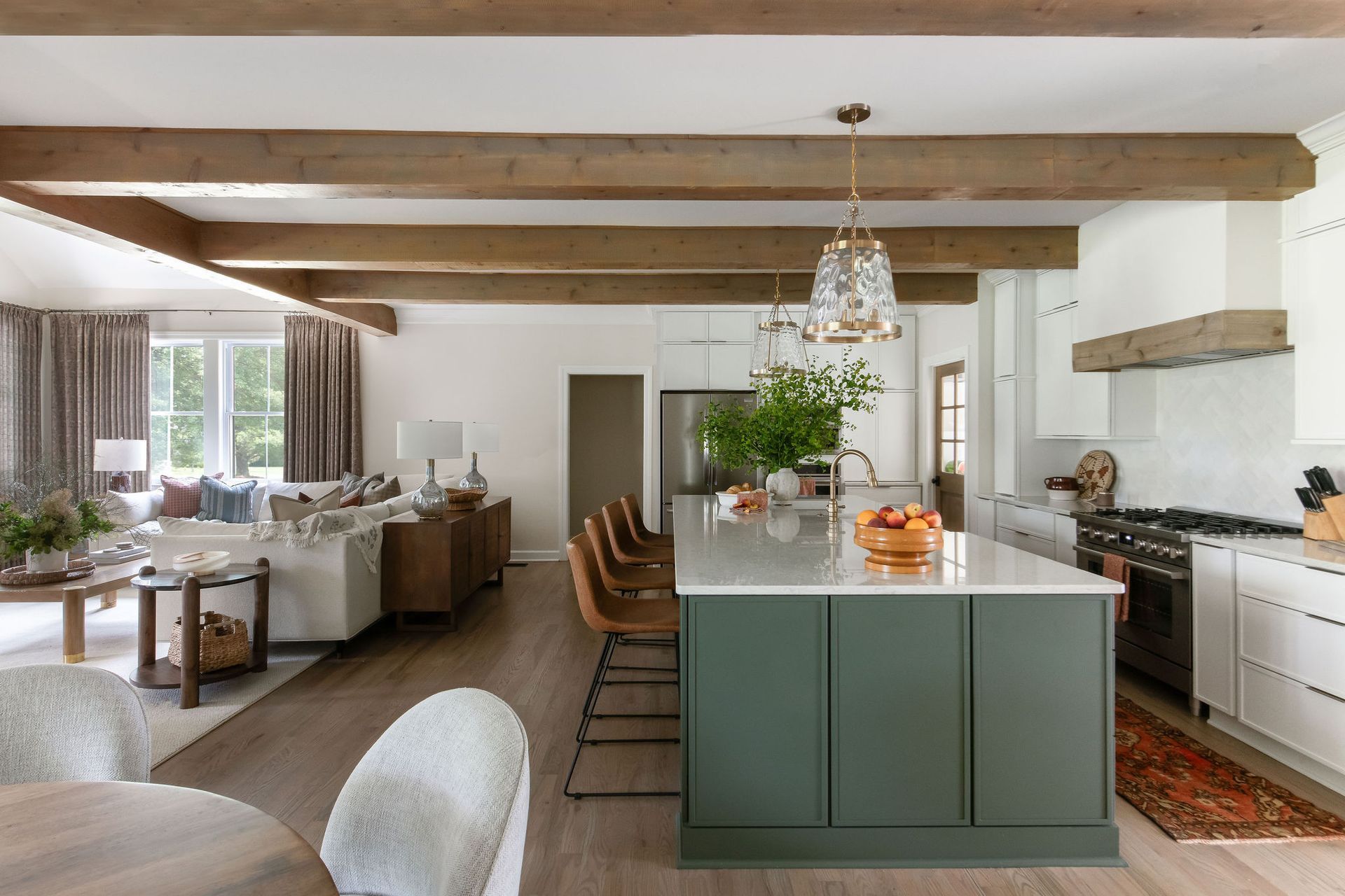 Open-concept kitchen and living area with wood beams, green island, and white cabinets.