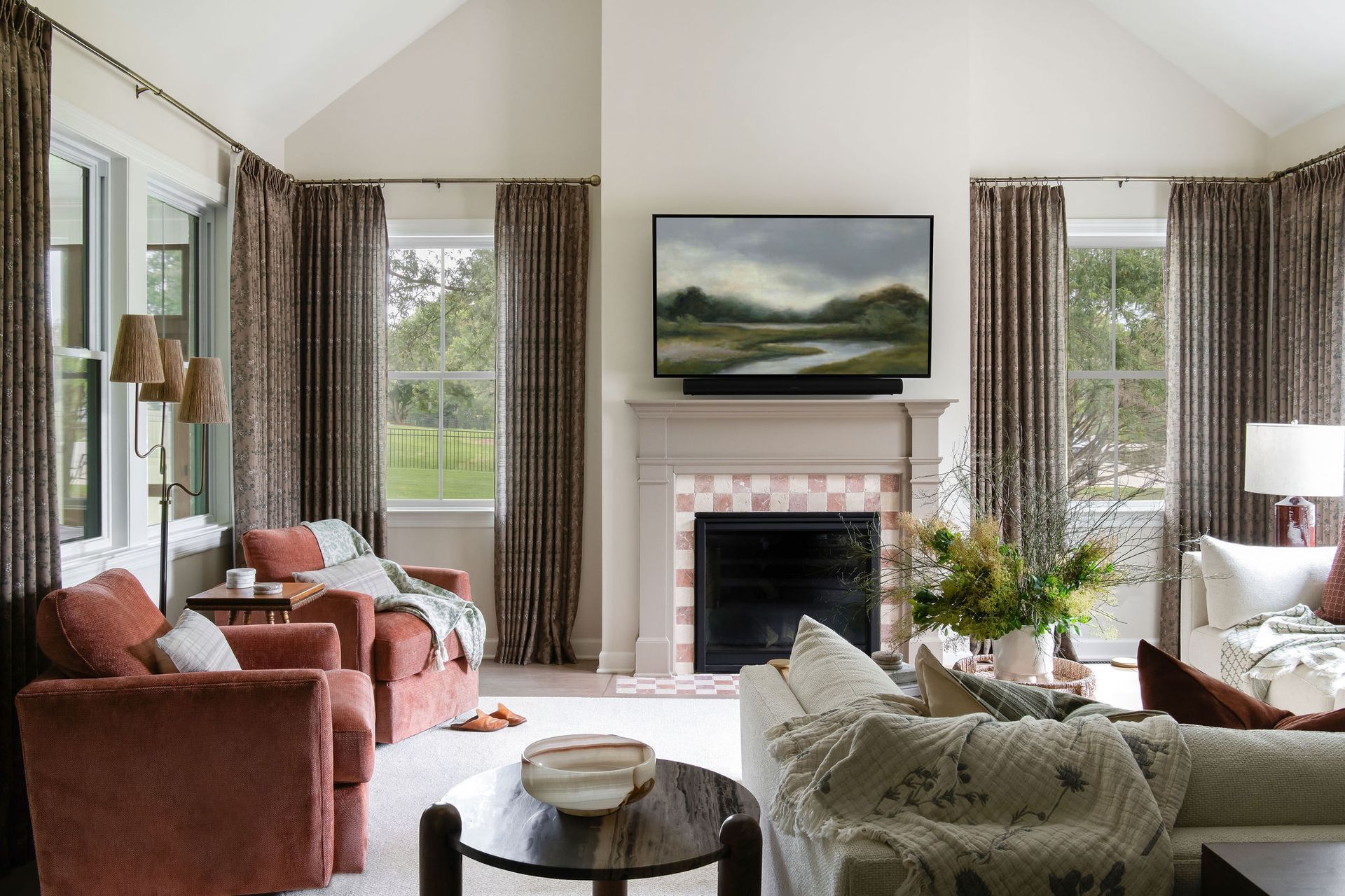 Living room with rust-colored chairs, a fireplace, large windows, and brown patterned curtains.