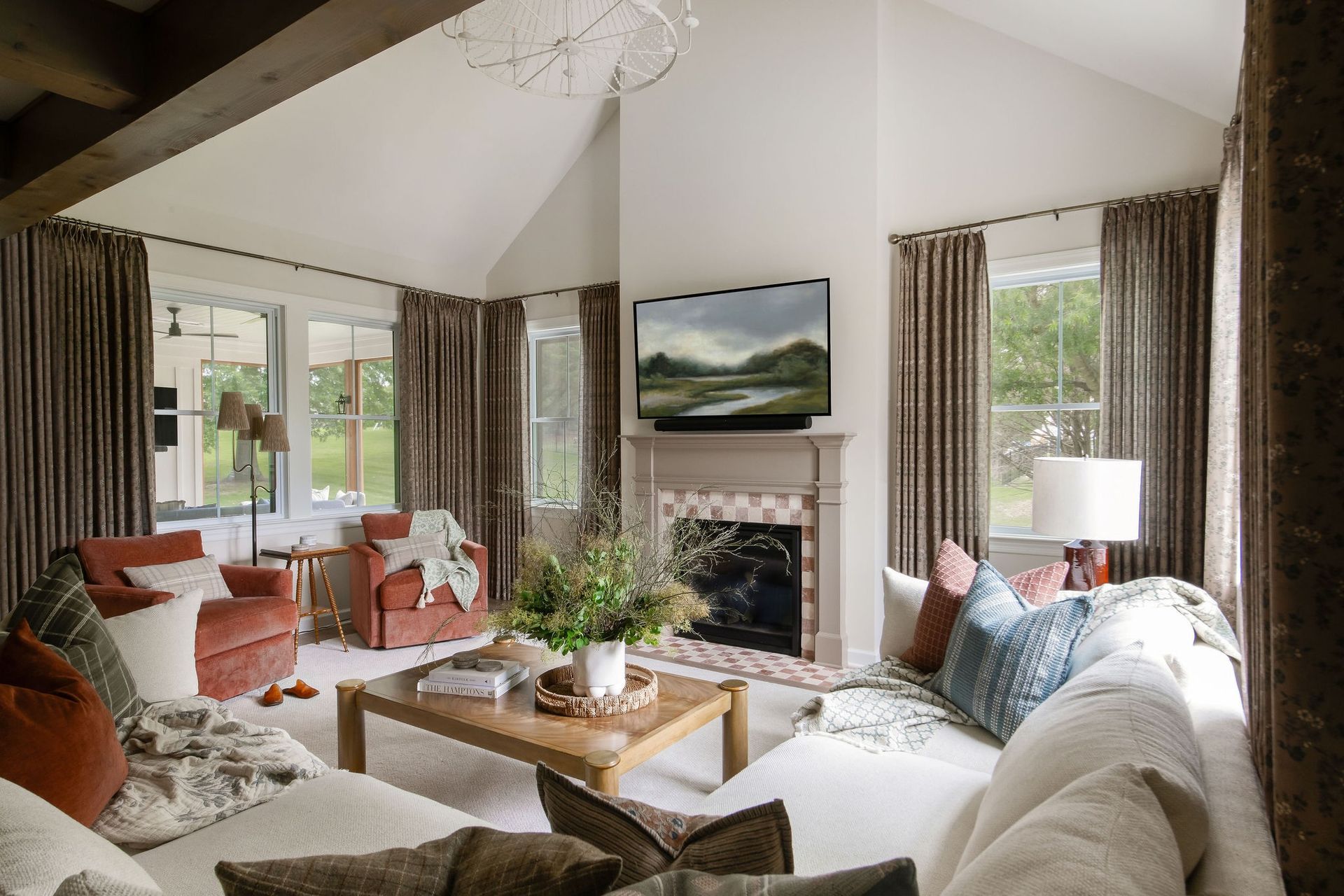 Bright living room with a vaulted ceiling, white sofa, fireplace, and large windows overlooking greenery