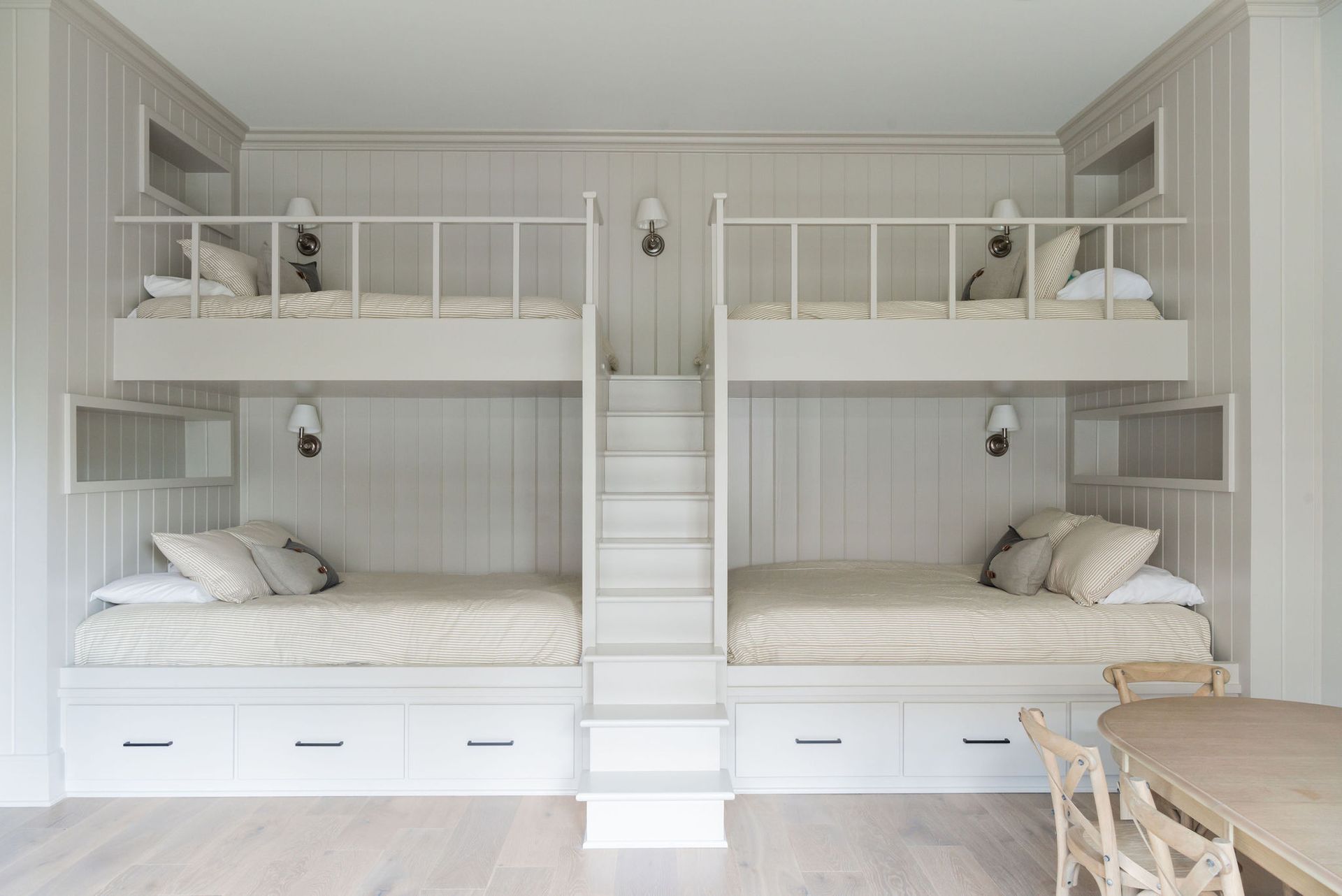Two sets of built-in bunk beds in a neutral-toned room with a ladder in the middle.