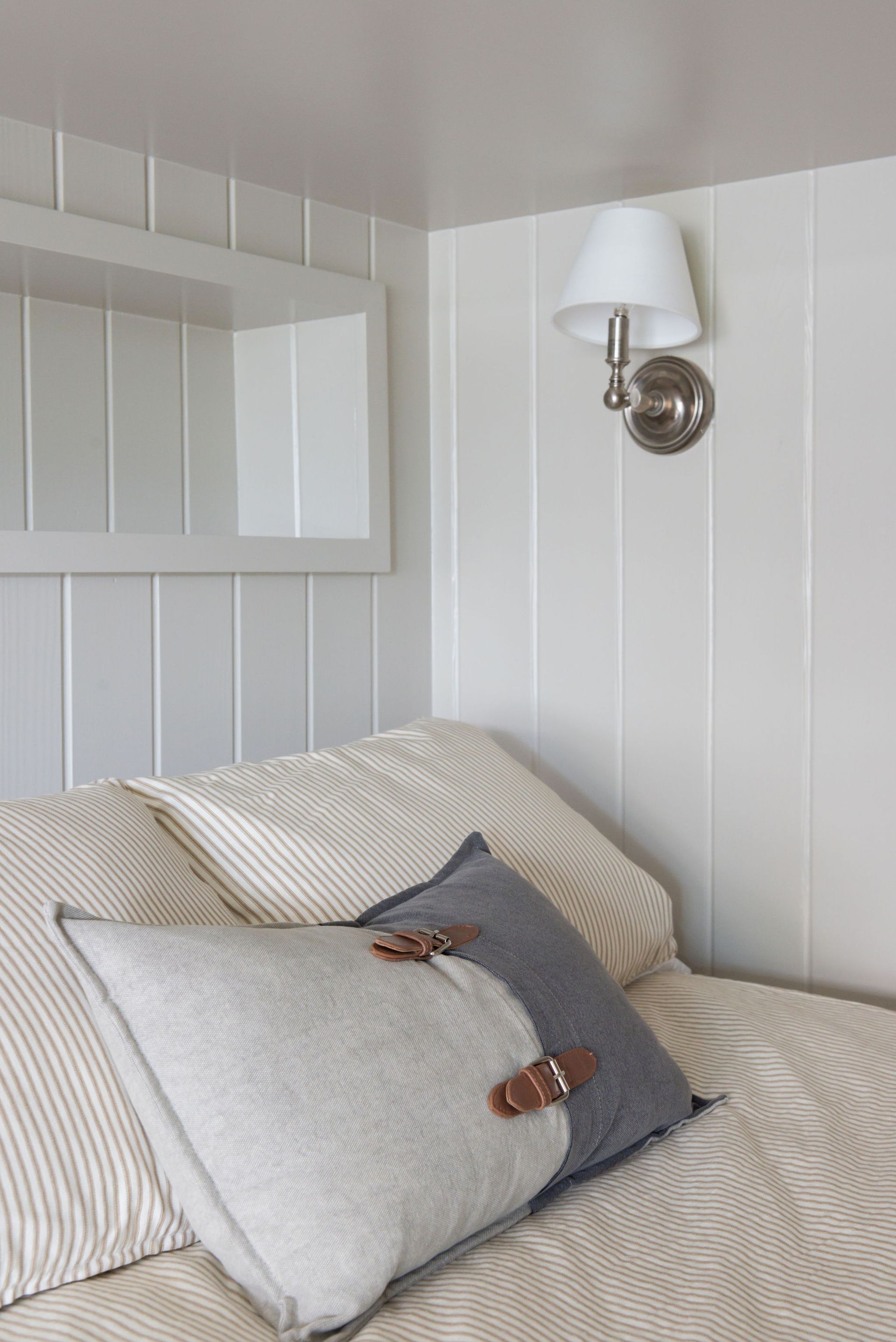 White bedroom corner with pillows, bed, wall lamp, and a built-in shelf.