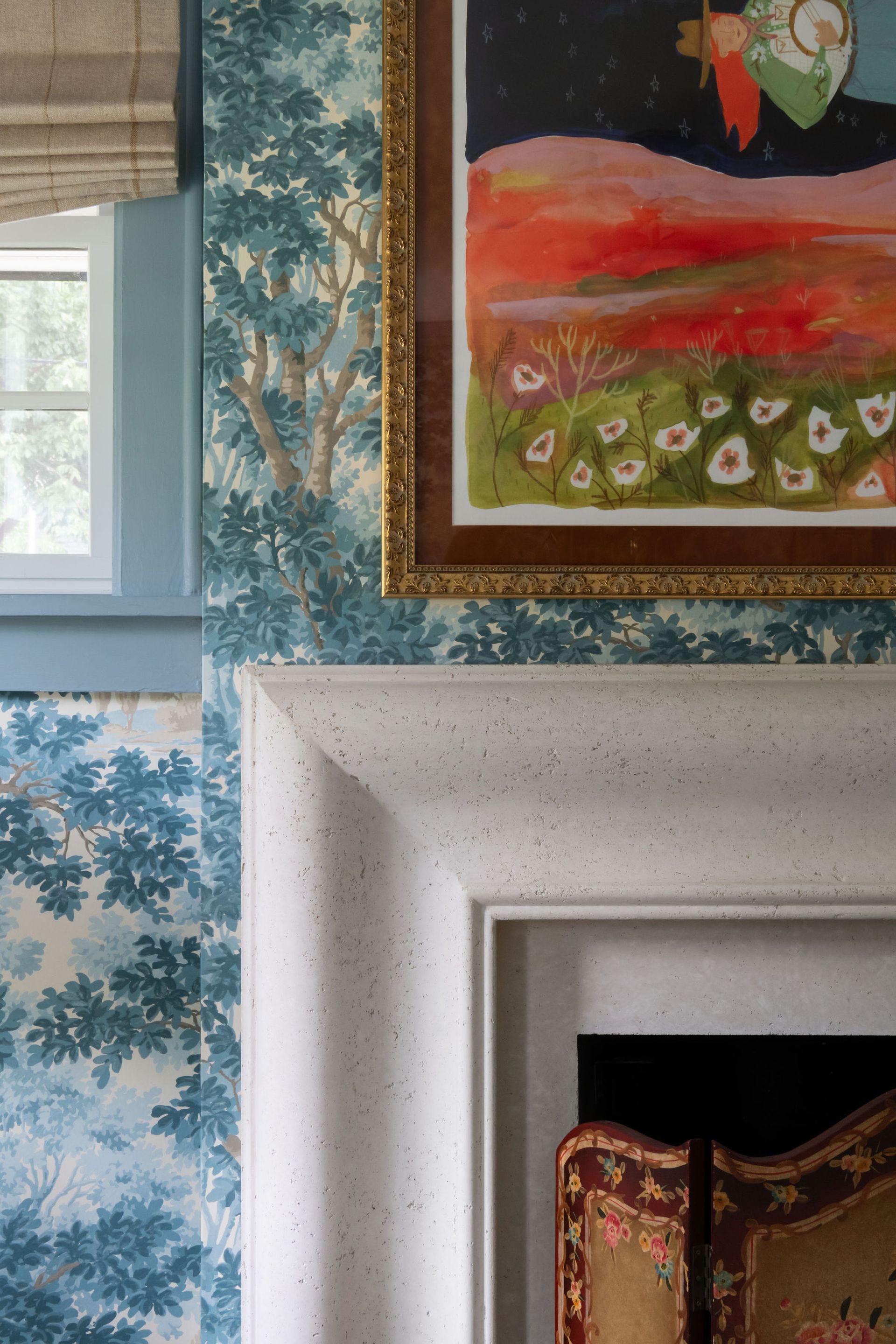Blue tree wallpaper, white fireplace, framed artwork, and a small window.