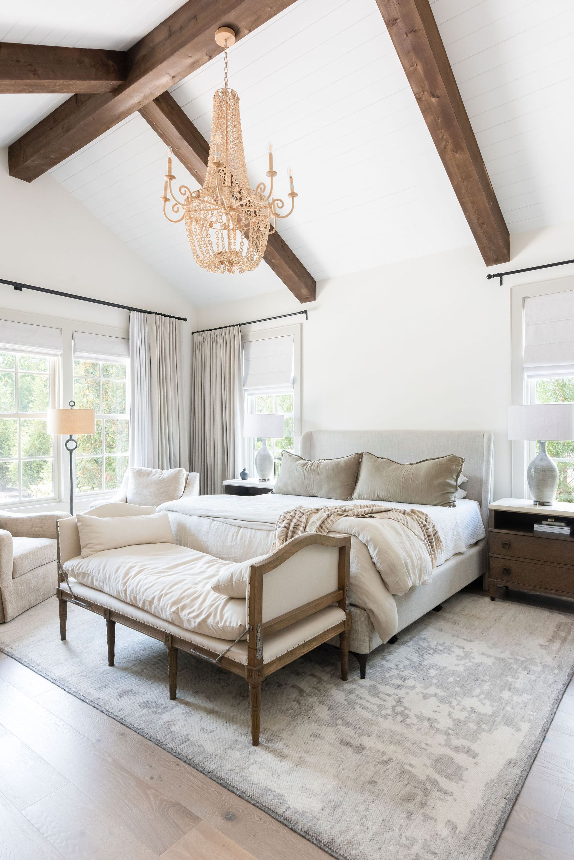 A bedroom with a large bed , a bench , and a chandelier.