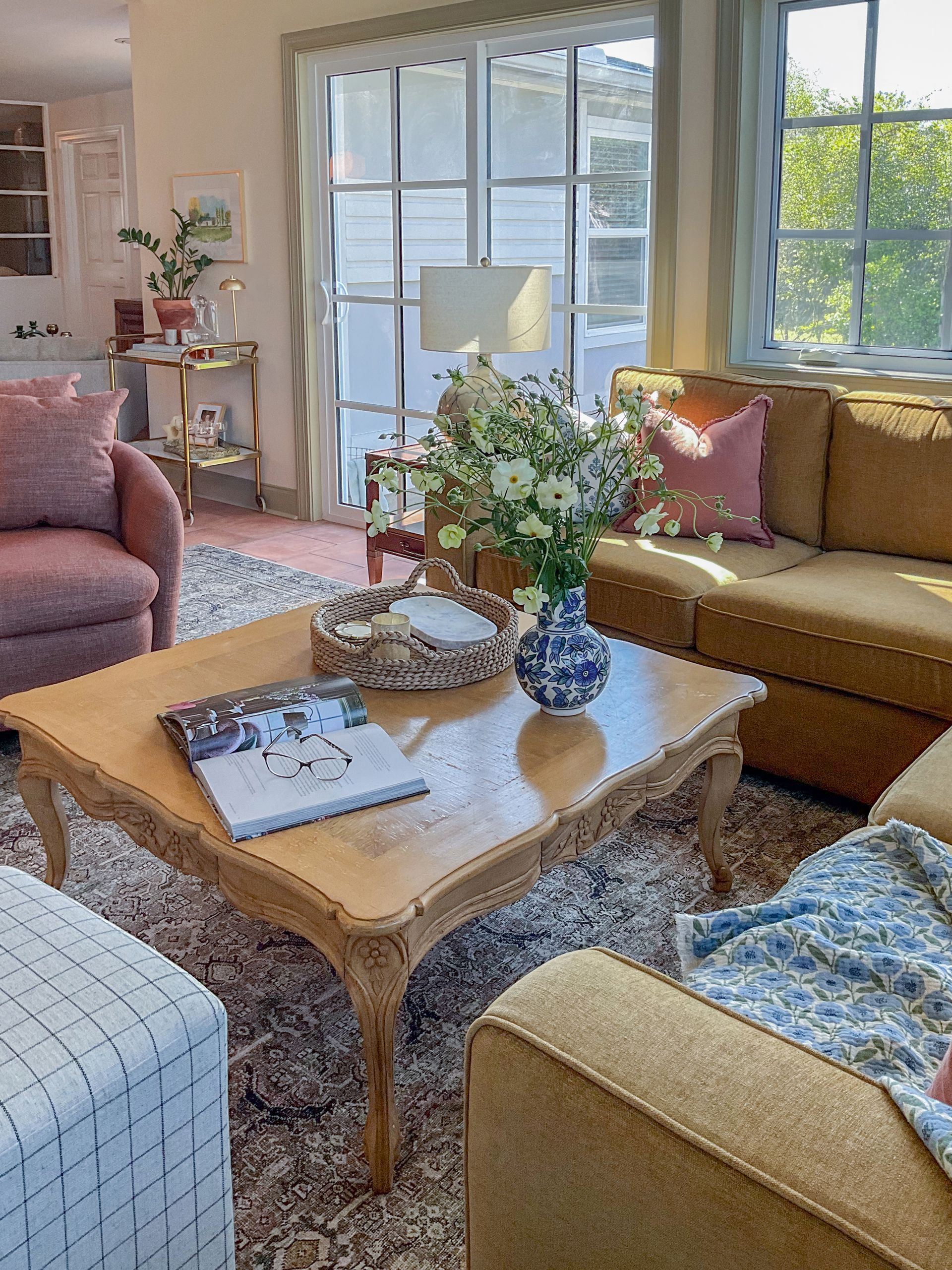 Living room with tan couch, pink armchair, and coffee table, floral arrangements.