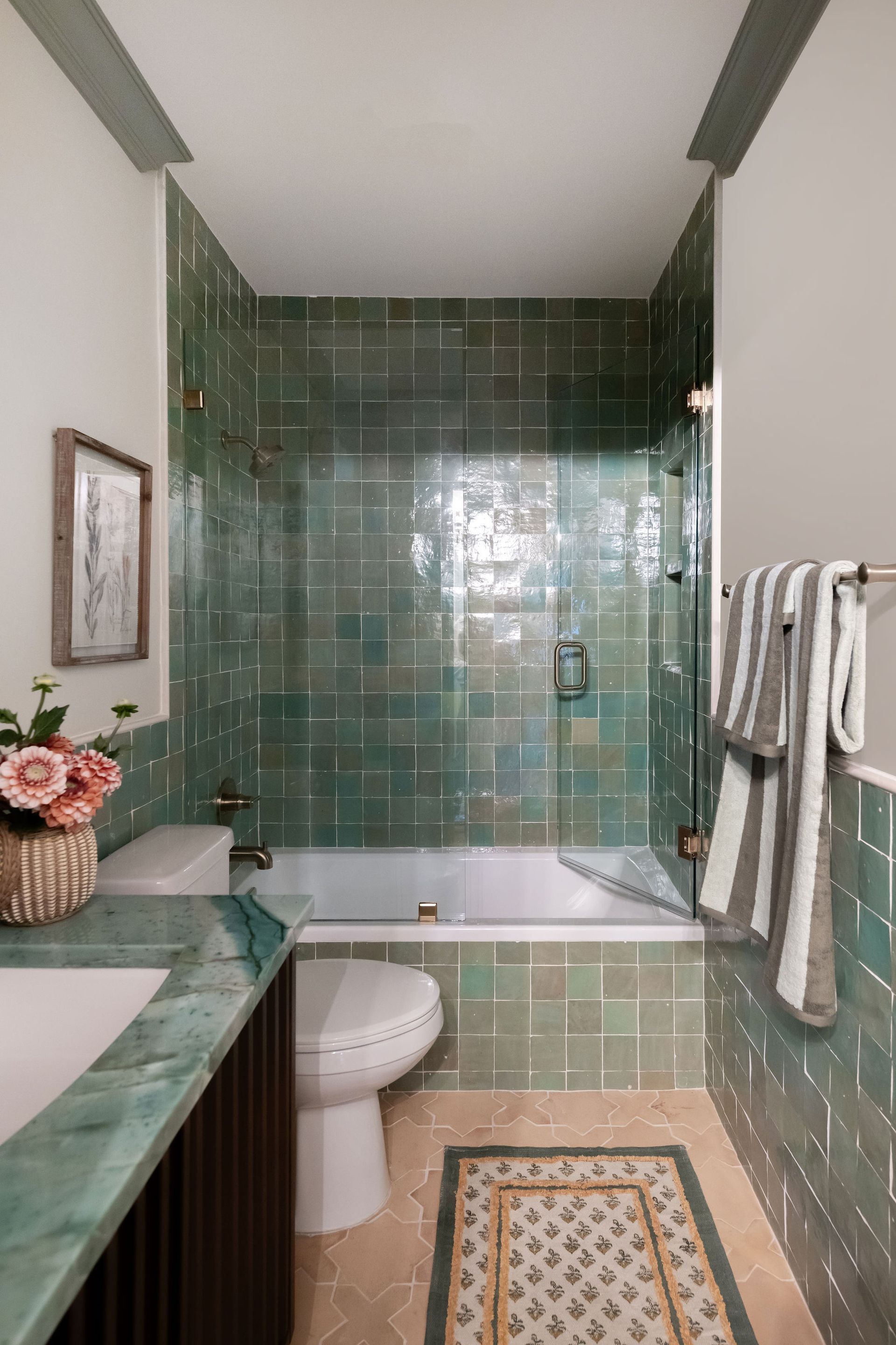 A small bathroom with green tiled walls and a tub/shower, next to a toilet and sink.