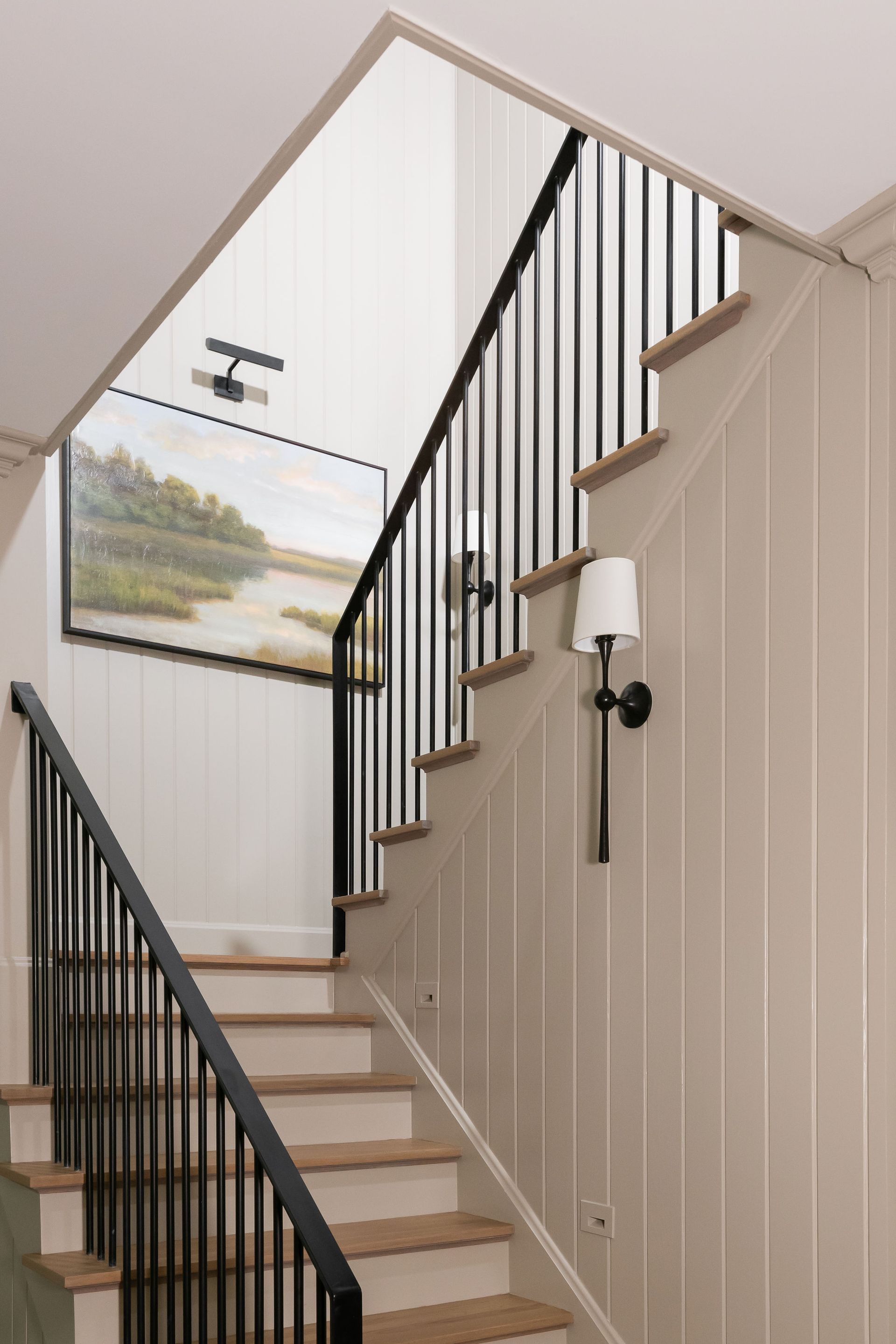 Staircase with black railing, beige wood paneling, and a landscape painting.