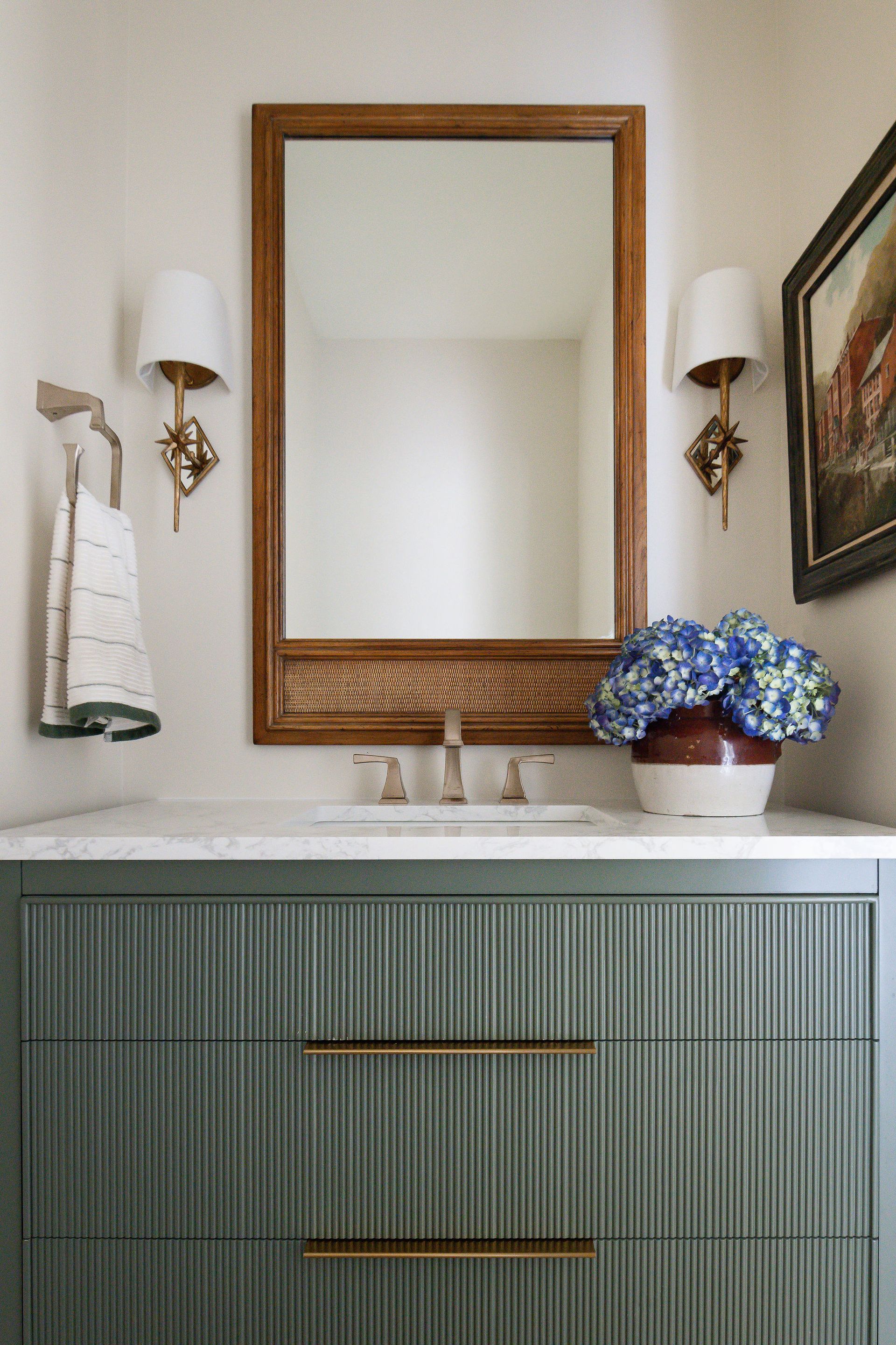 Bathroom with a sage green vanity, gold accents, and a brown framed mirror.