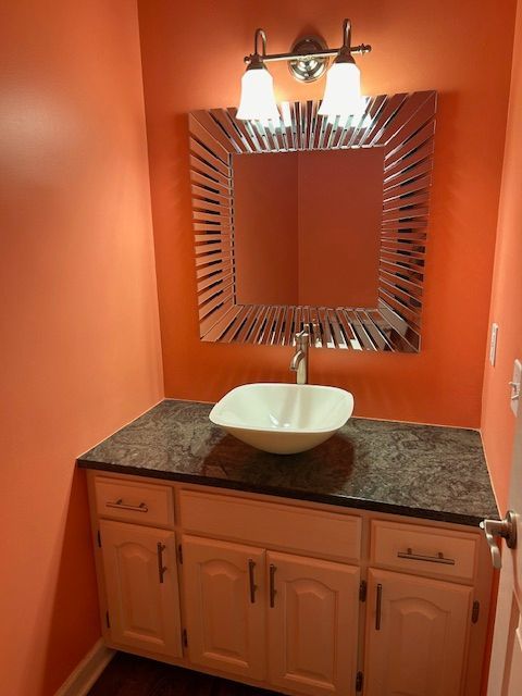Peach-walled powder room with a white sink, a decorative mirror, and a granite countertop.