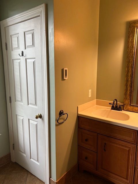 Bathroom with a white door, vanity, and a gold-framed mirror. Light brown walls and wood-toned cabinets.