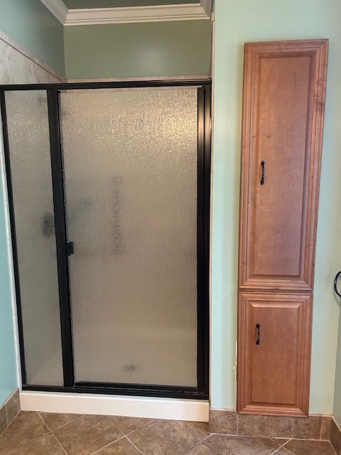 Bathroom with shower and tall cabinet; shower has frosted glass doors and black frame; light brown cabinet.