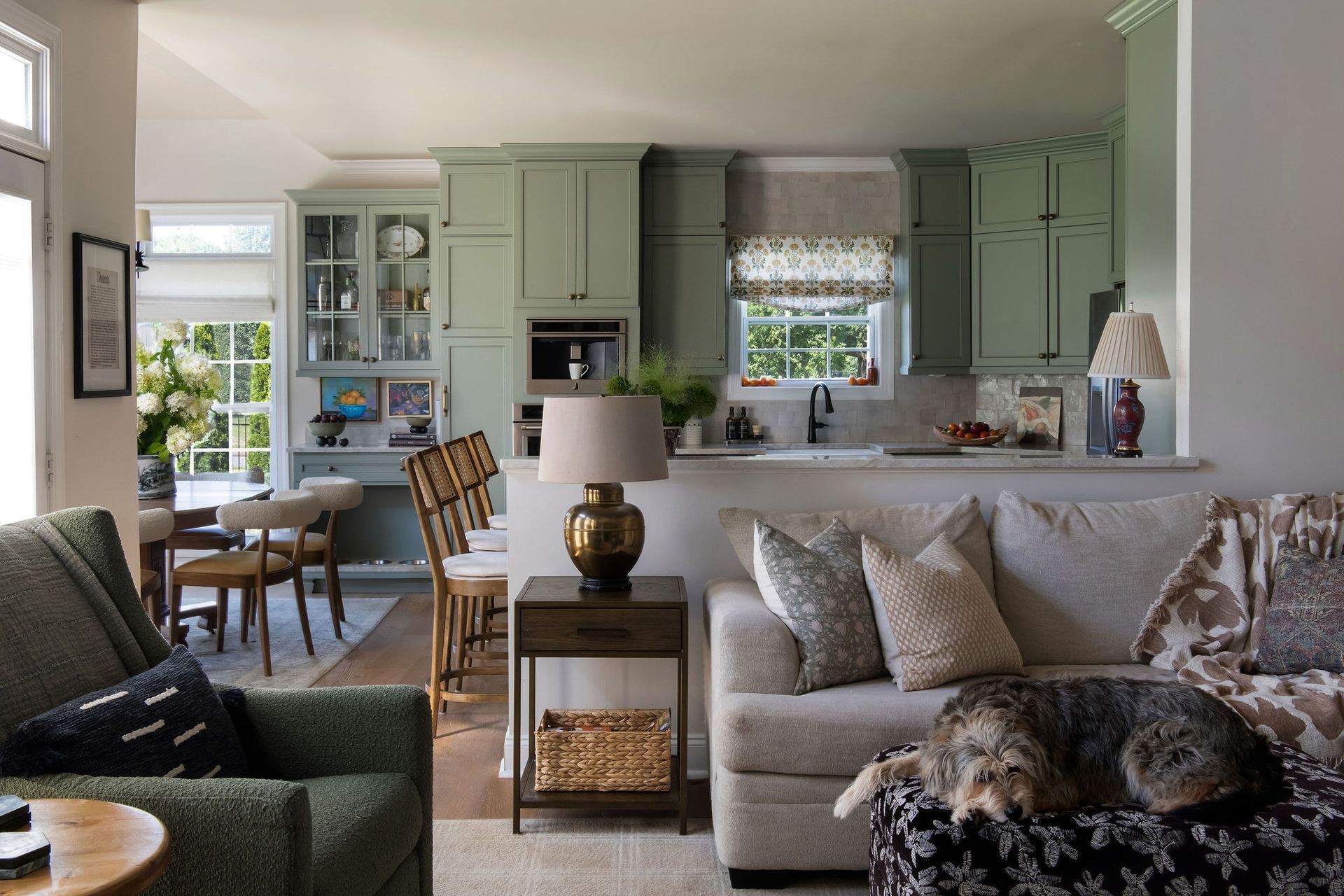 Bright living room with green cabinets, a gray sofa, and a dog resting on a patterned chair.