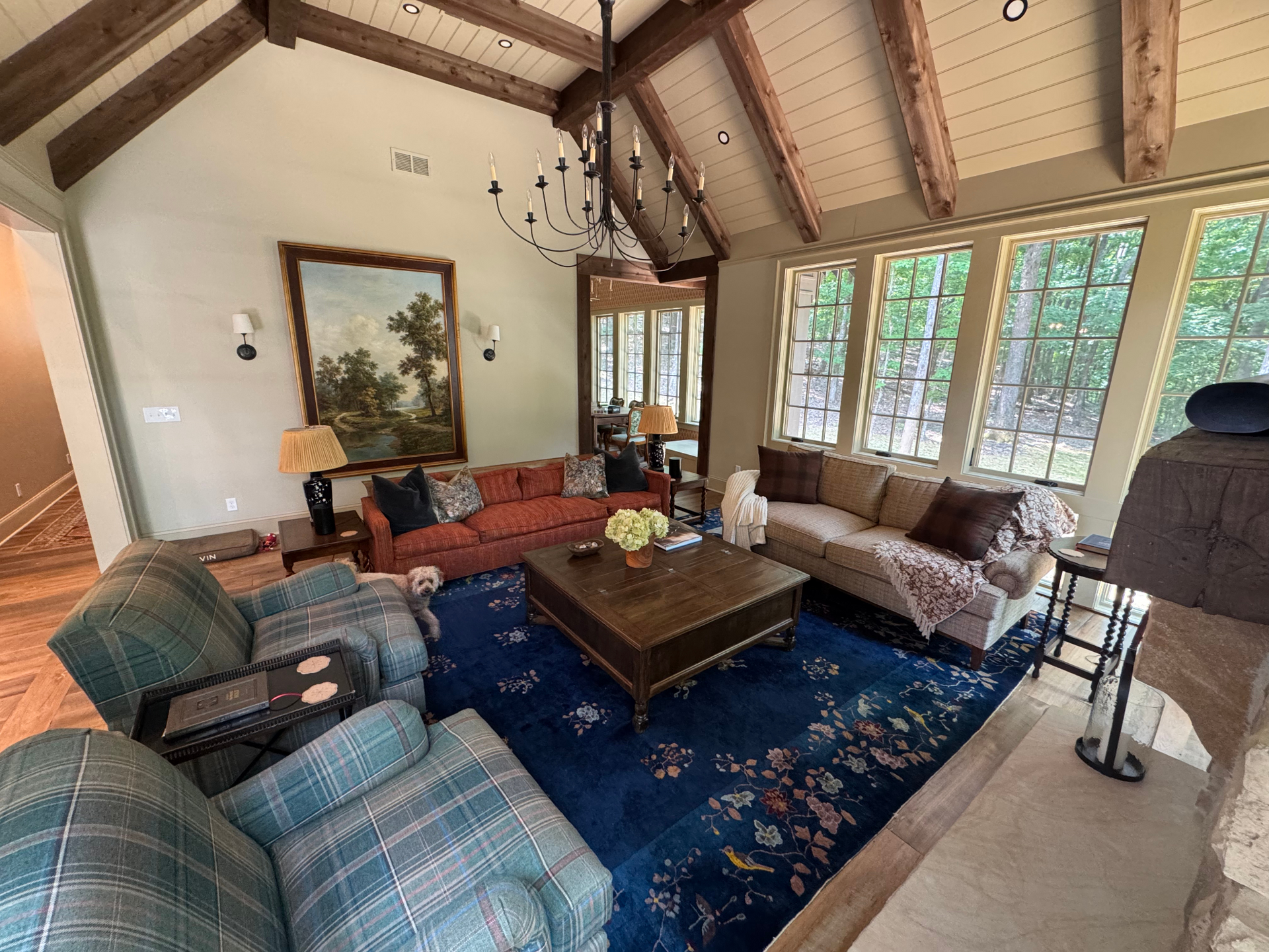 Cozy living room with vaulted ceiling, exposed beams, and blue patterned rug. Includes furniture and art.